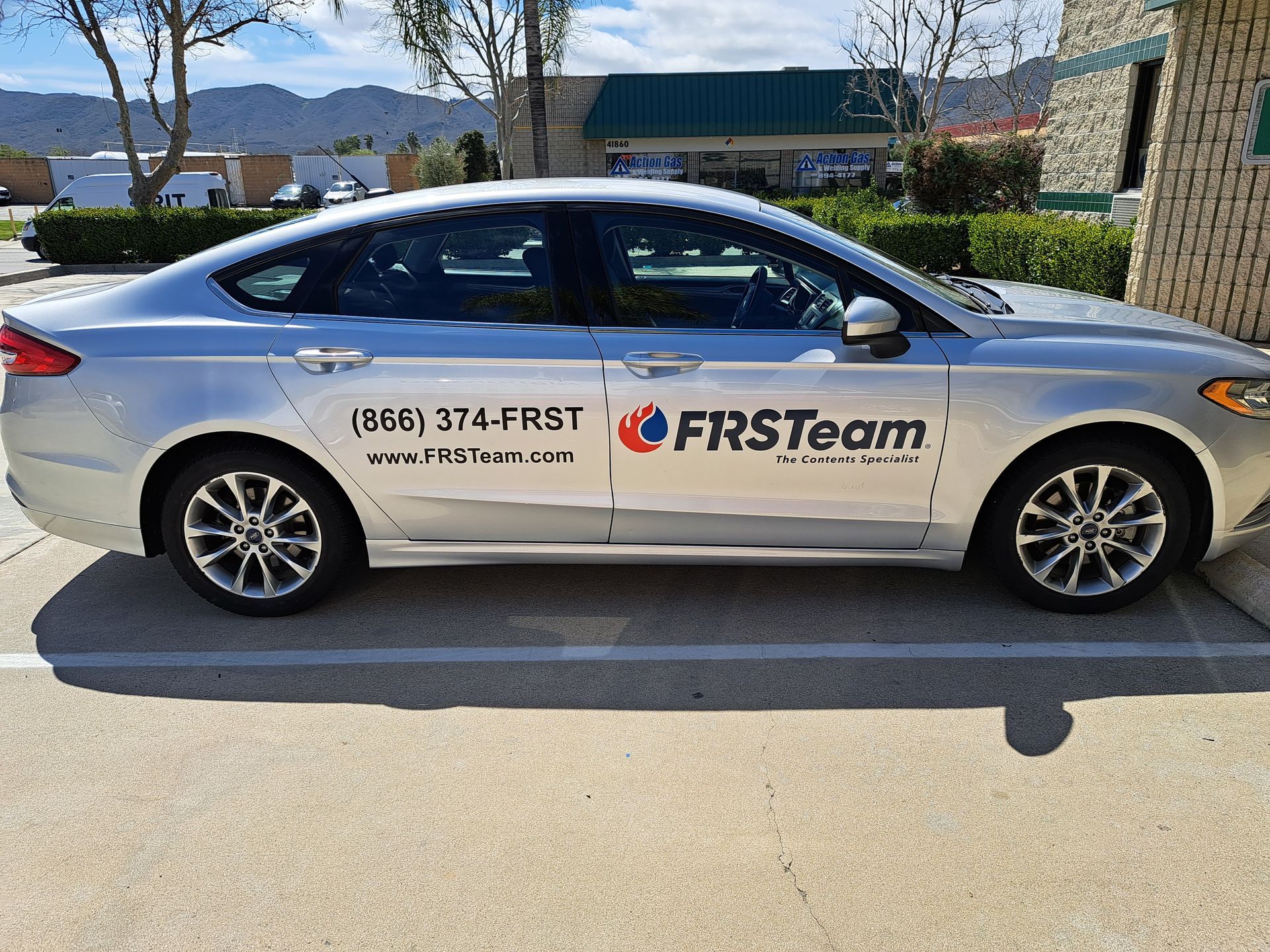 Silver FIRSTeam sedan with company logo and phone number parked outside a building