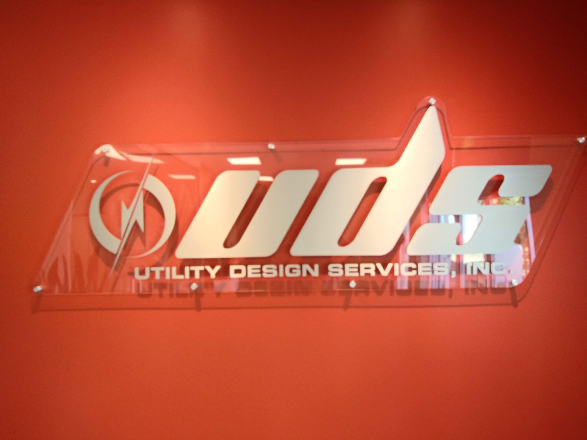Red wall with a chrome “uds” logo and the words “Utility Design Services” beneath it.
