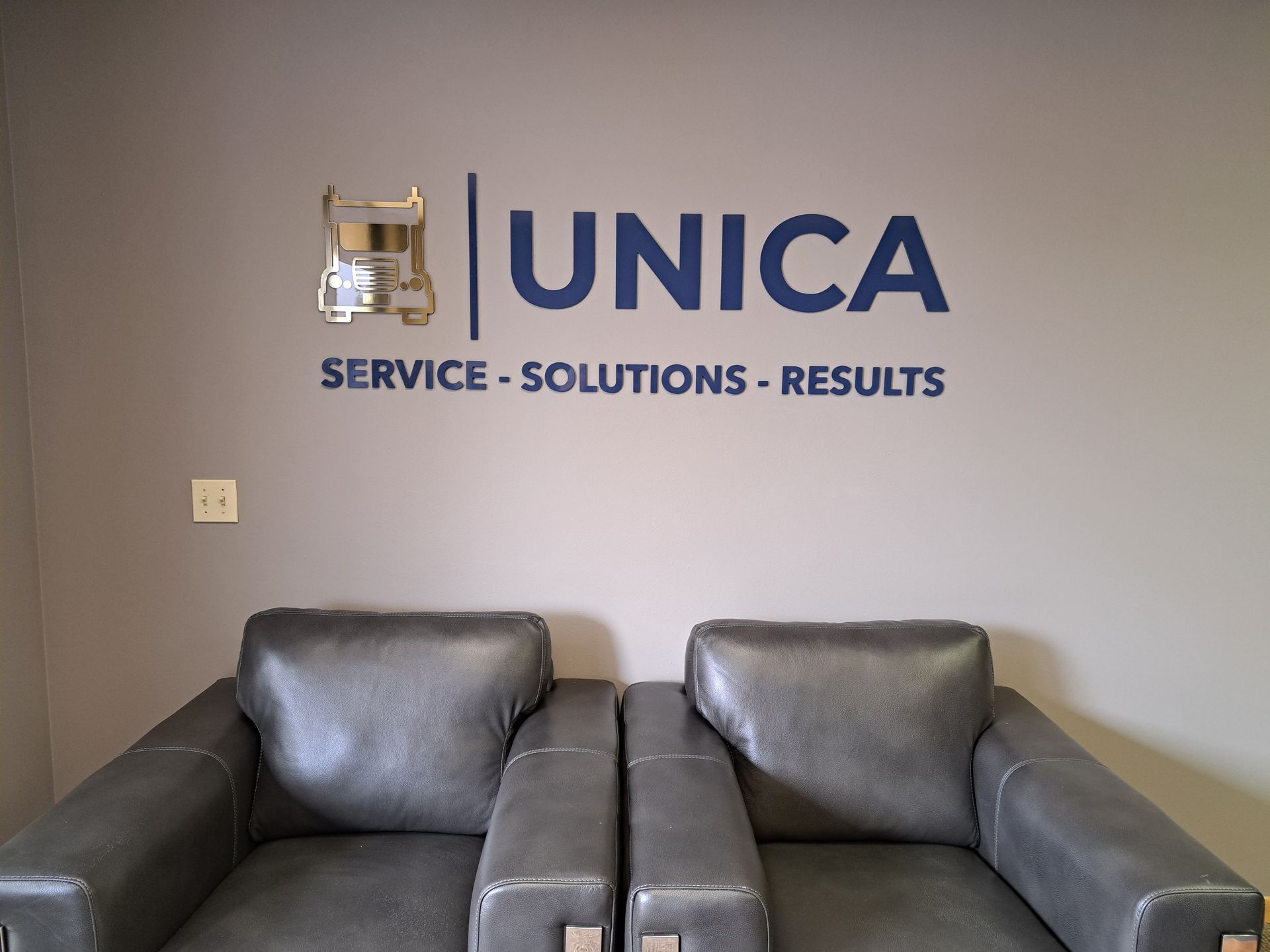 UNICA office wall logo above two gray leather sofas in a waiting area