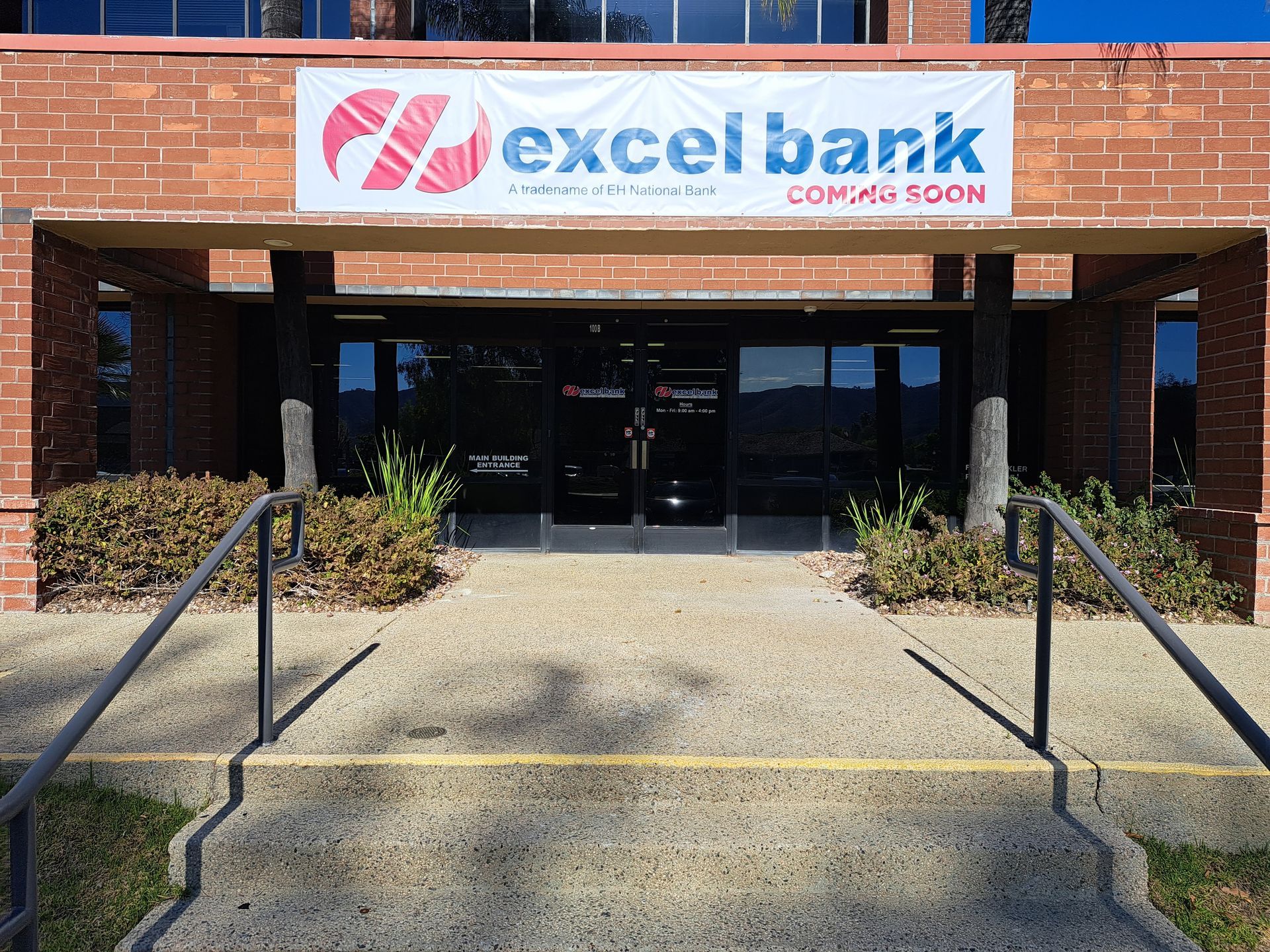 Closed Excel Bank entrance with brick facade, glass doors, and steps with black handrails.