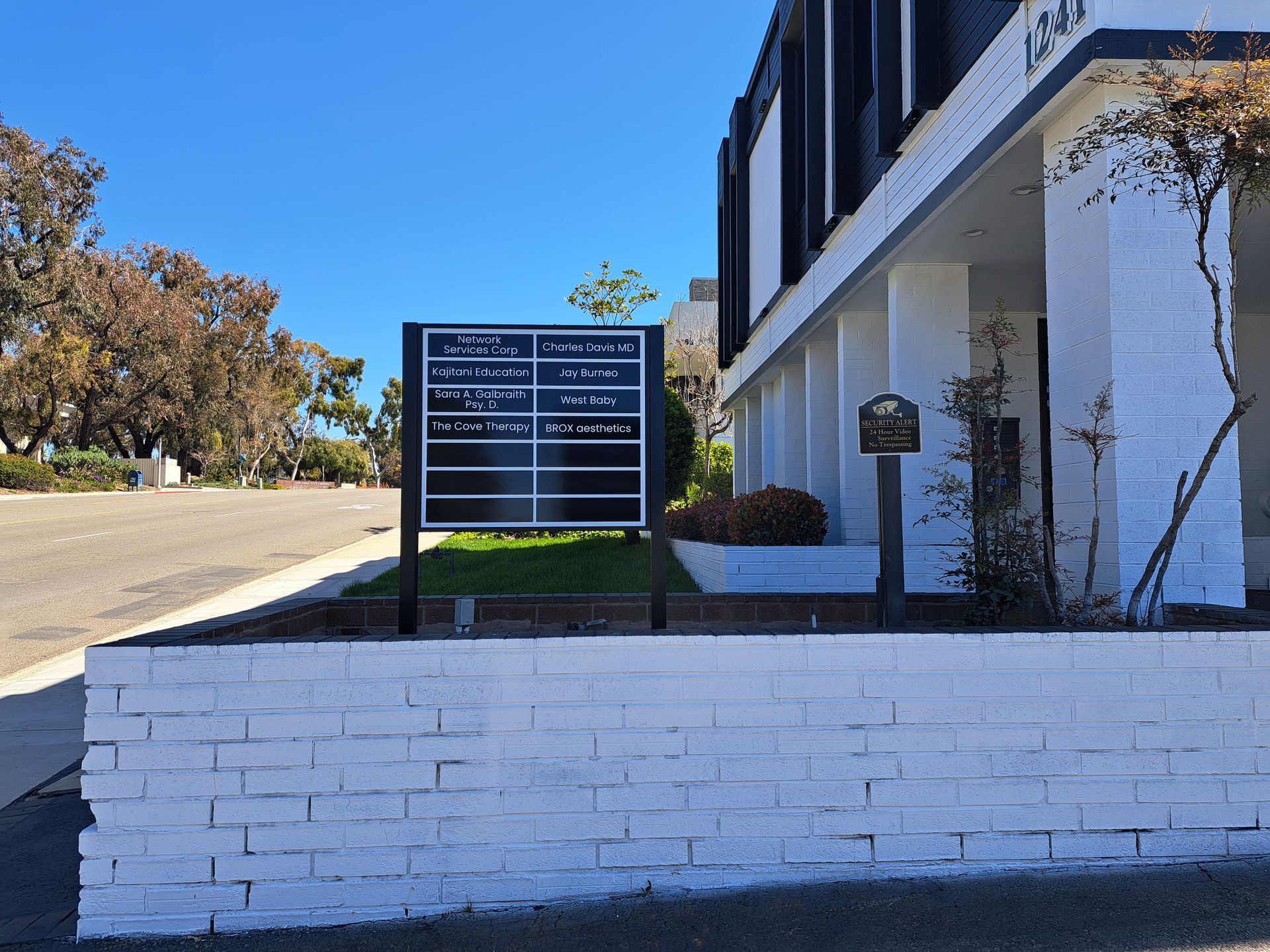 Office building with a black directory sign and white brick wall beside a sloped road