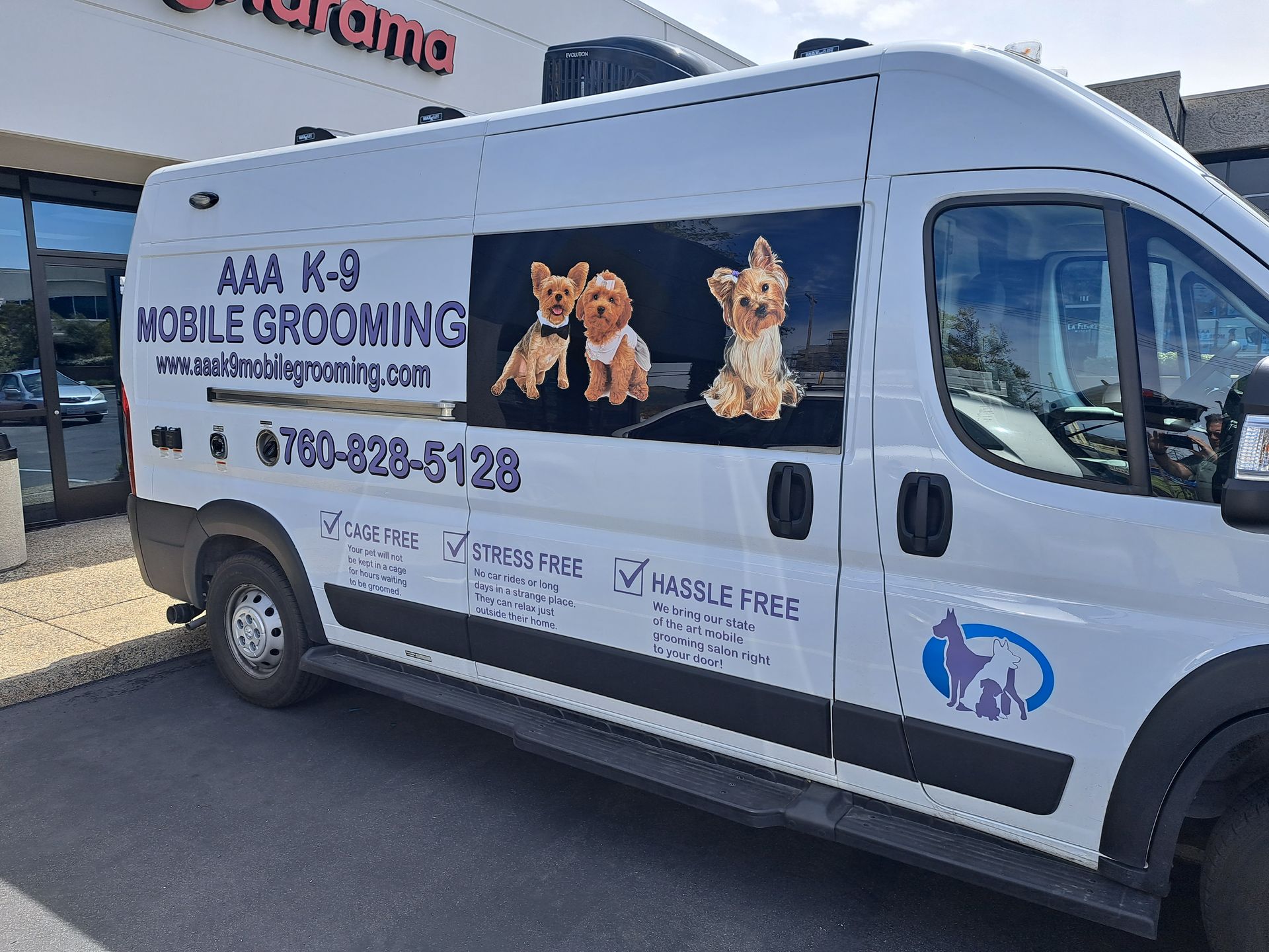 White mobile pet grooming van with dog graphics and business branding parked outside a building