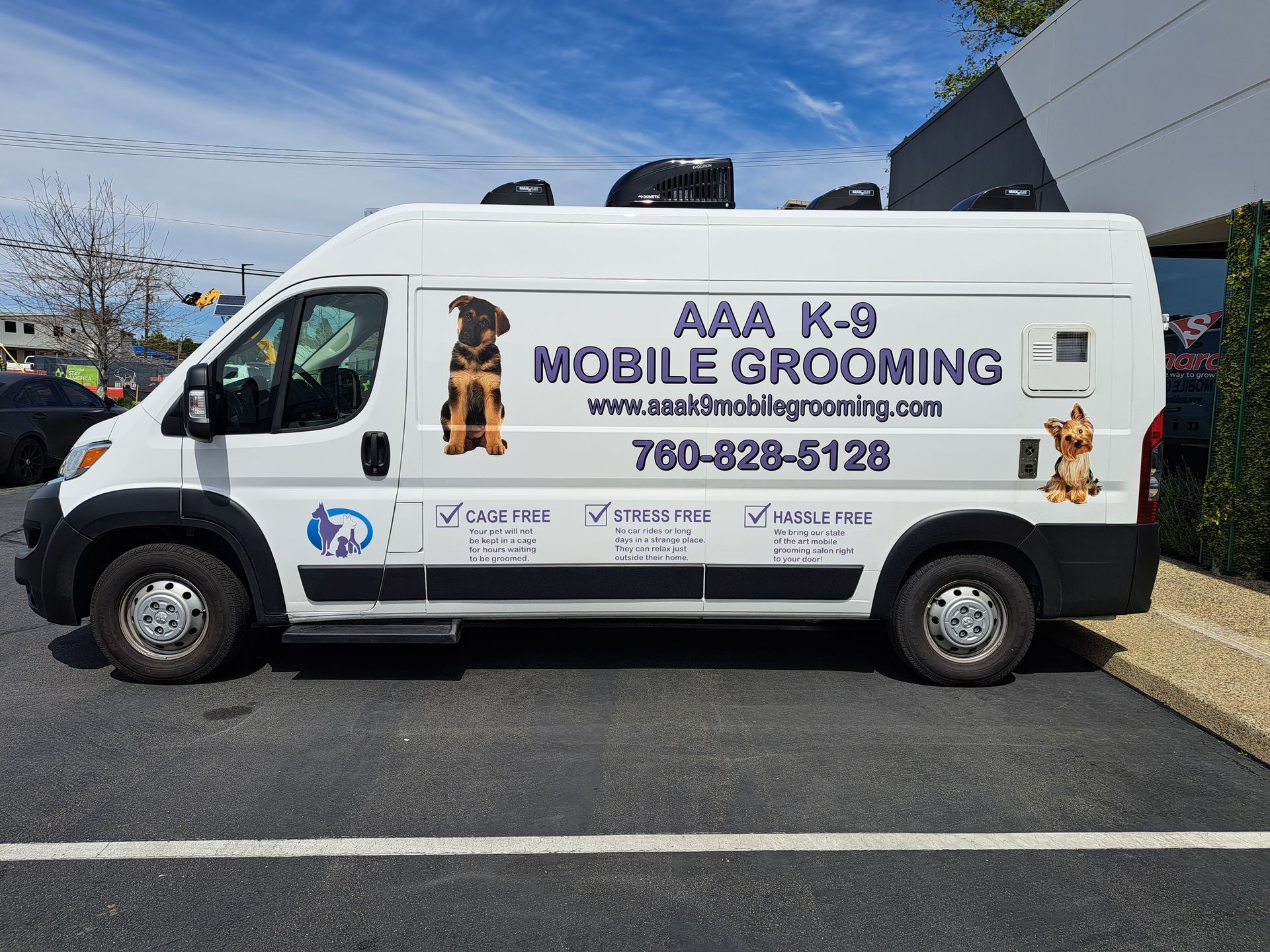 White mobile pet grooming van parked outdoors with “AKB K-9 MOBILE GROOMING” signage and phone number.
