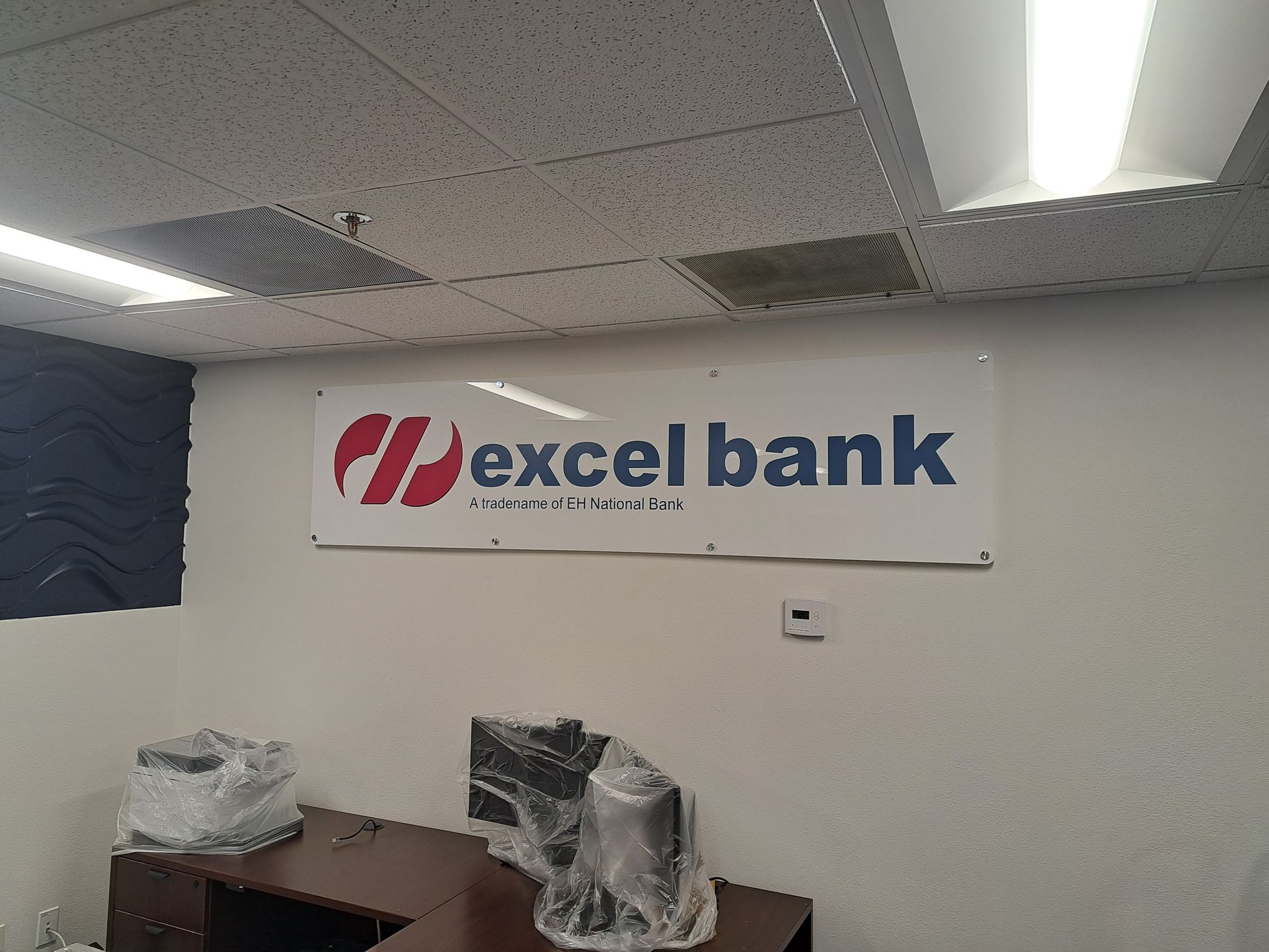 Excel Bank sign on an office wall with desks and ceiling lights underneath