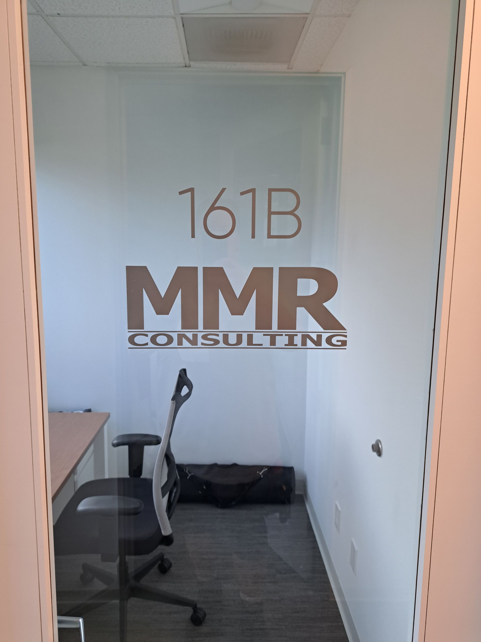 Office entrance with “161B MMR Consulting” logo on a white wall and two office chairs inside.