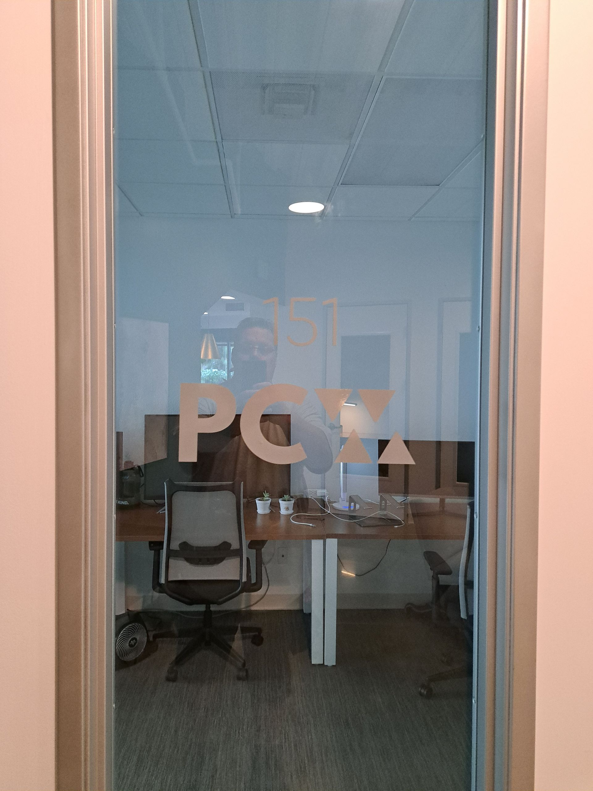 Office seen through glass door with frosted “PGA” lettering and a desk inside