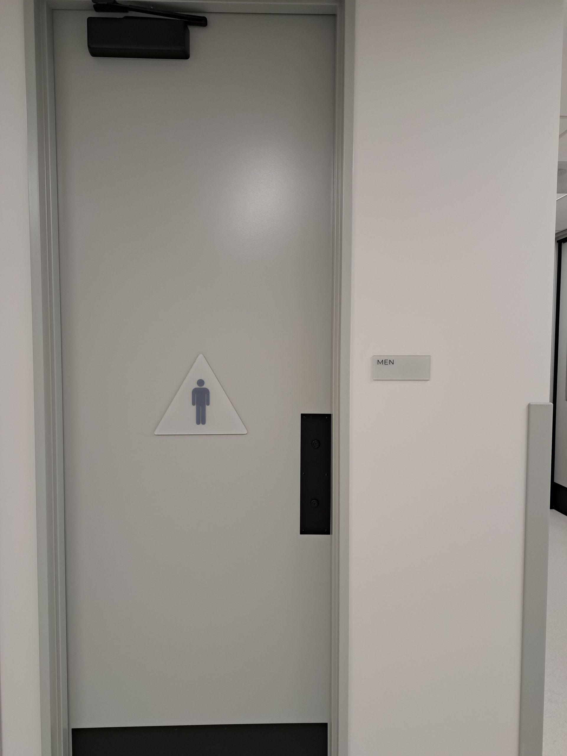 Closed gray restroom door with a unisex bathroom sign and wall plaque