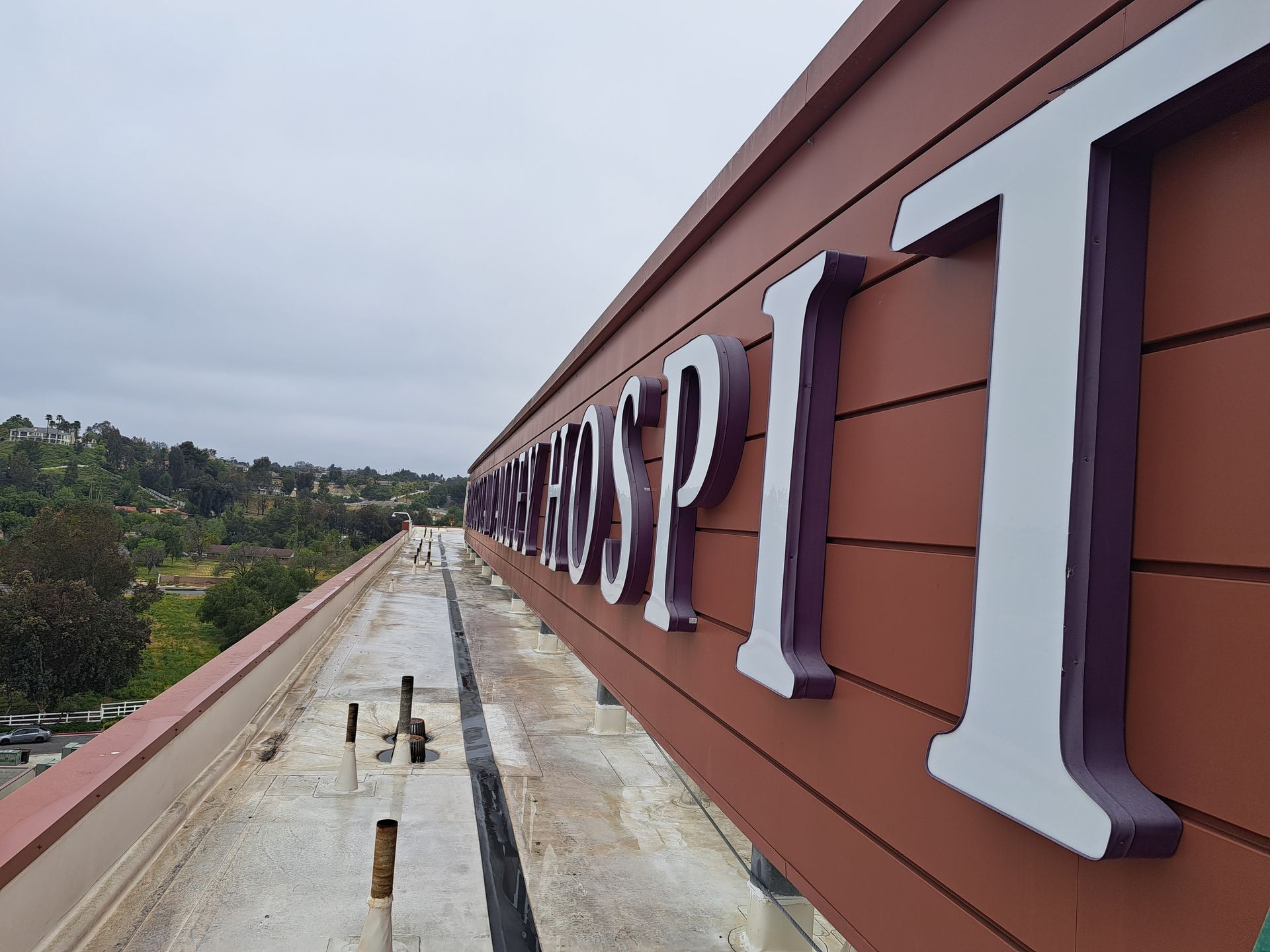 Close-up of large white letters on a brown rooftop sign along a long building walkway.