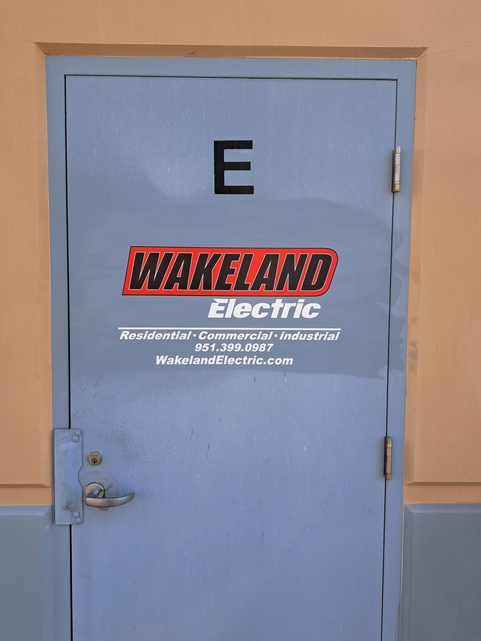 Light blue metal door with “E” and WakeLand Electric sign on a tan wall