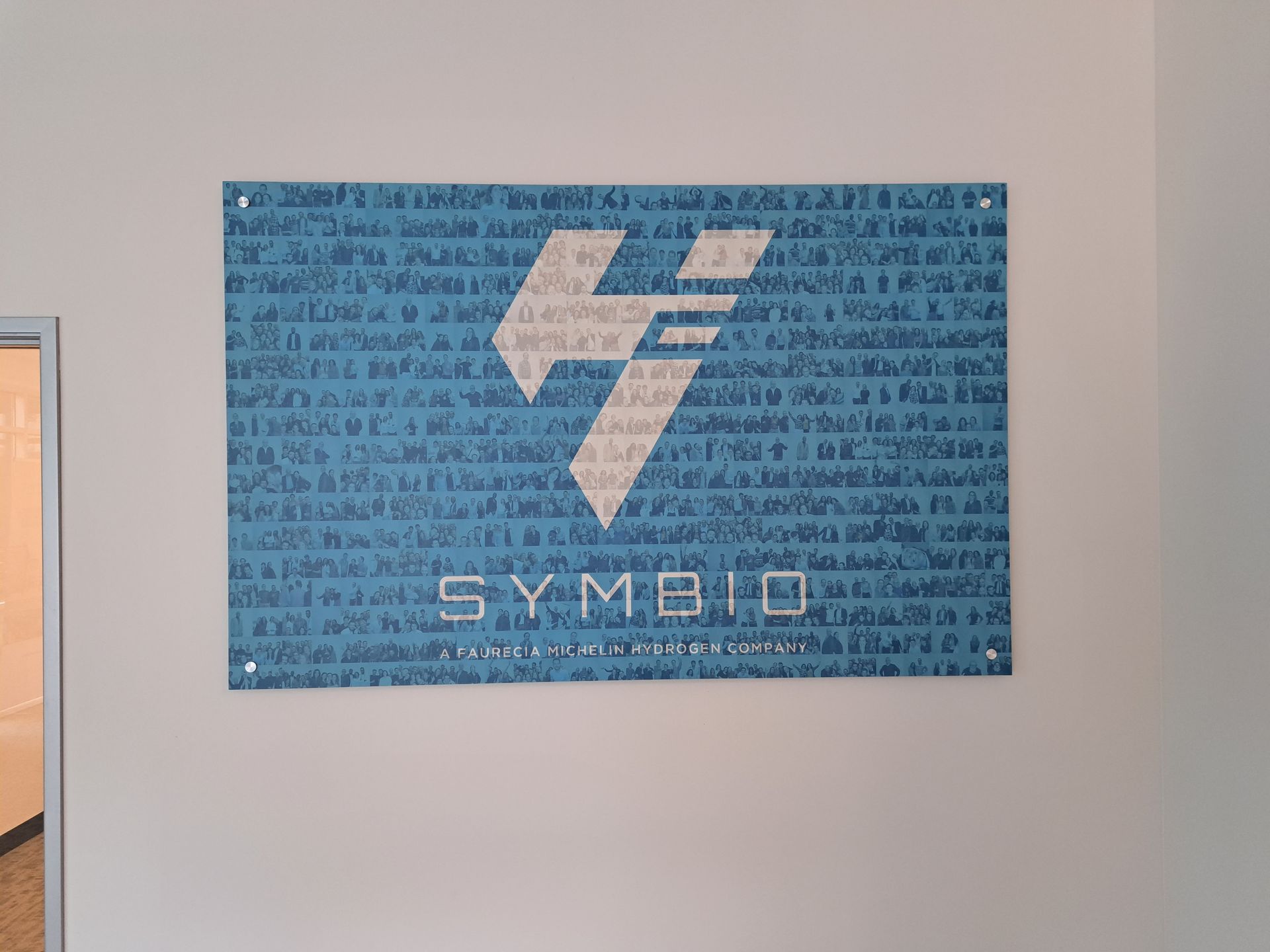 Blue SYMBIO banner with a white geometric logo on a wall