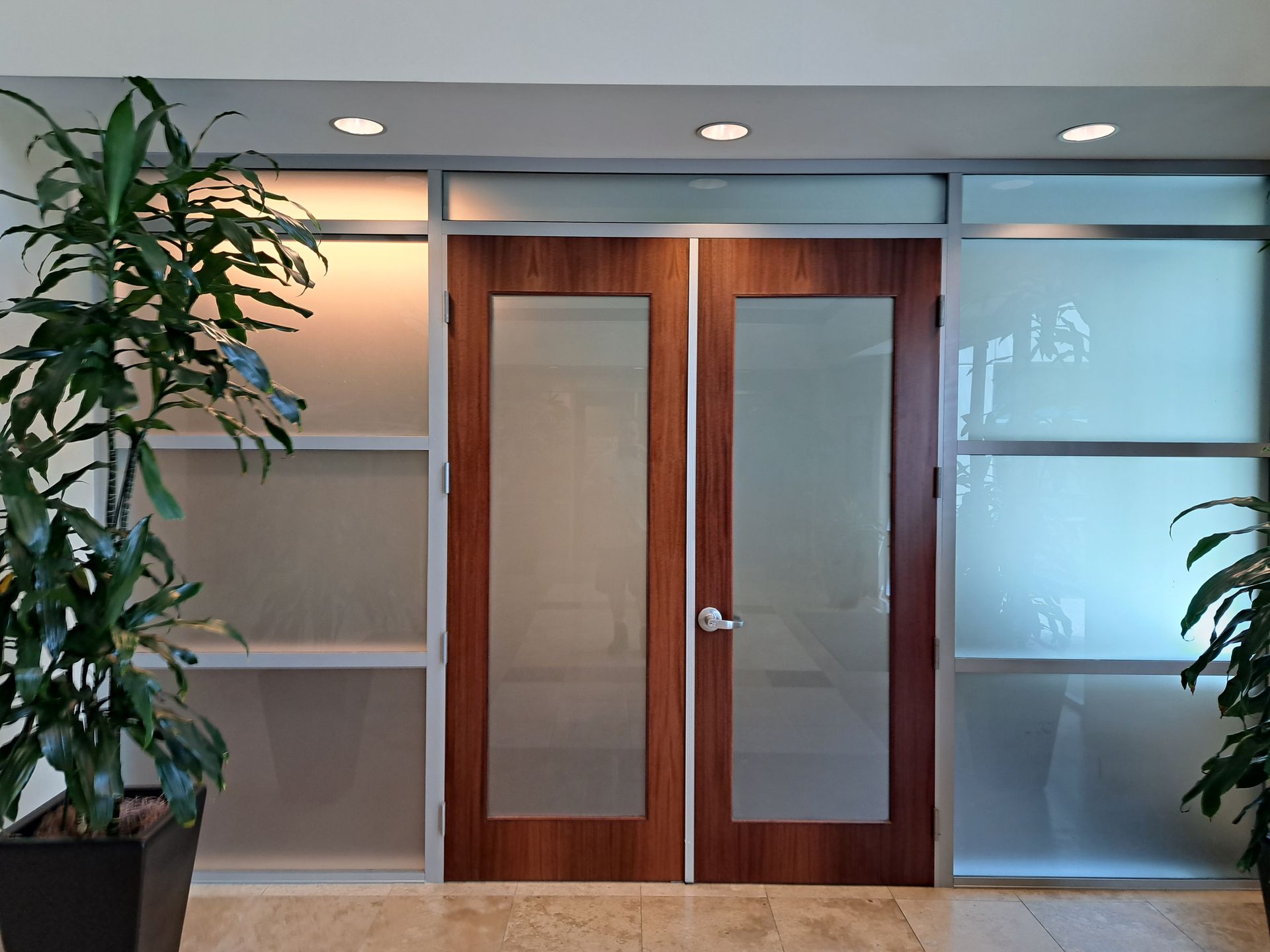 Office entrance with glass double doors, frosted side panels, and potted plants indoors