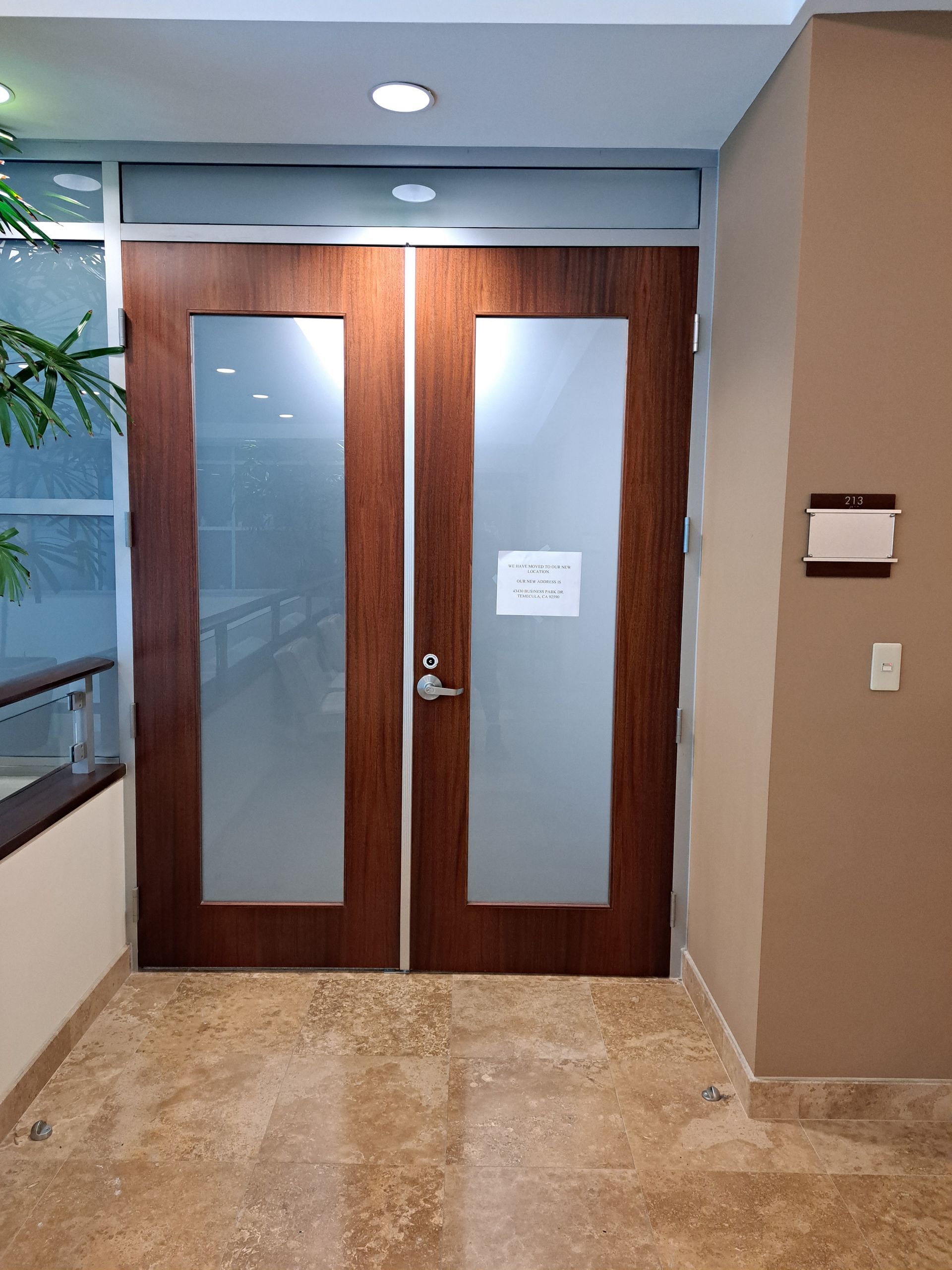 Wooden double doors with frosted glass panels in an office hallway.