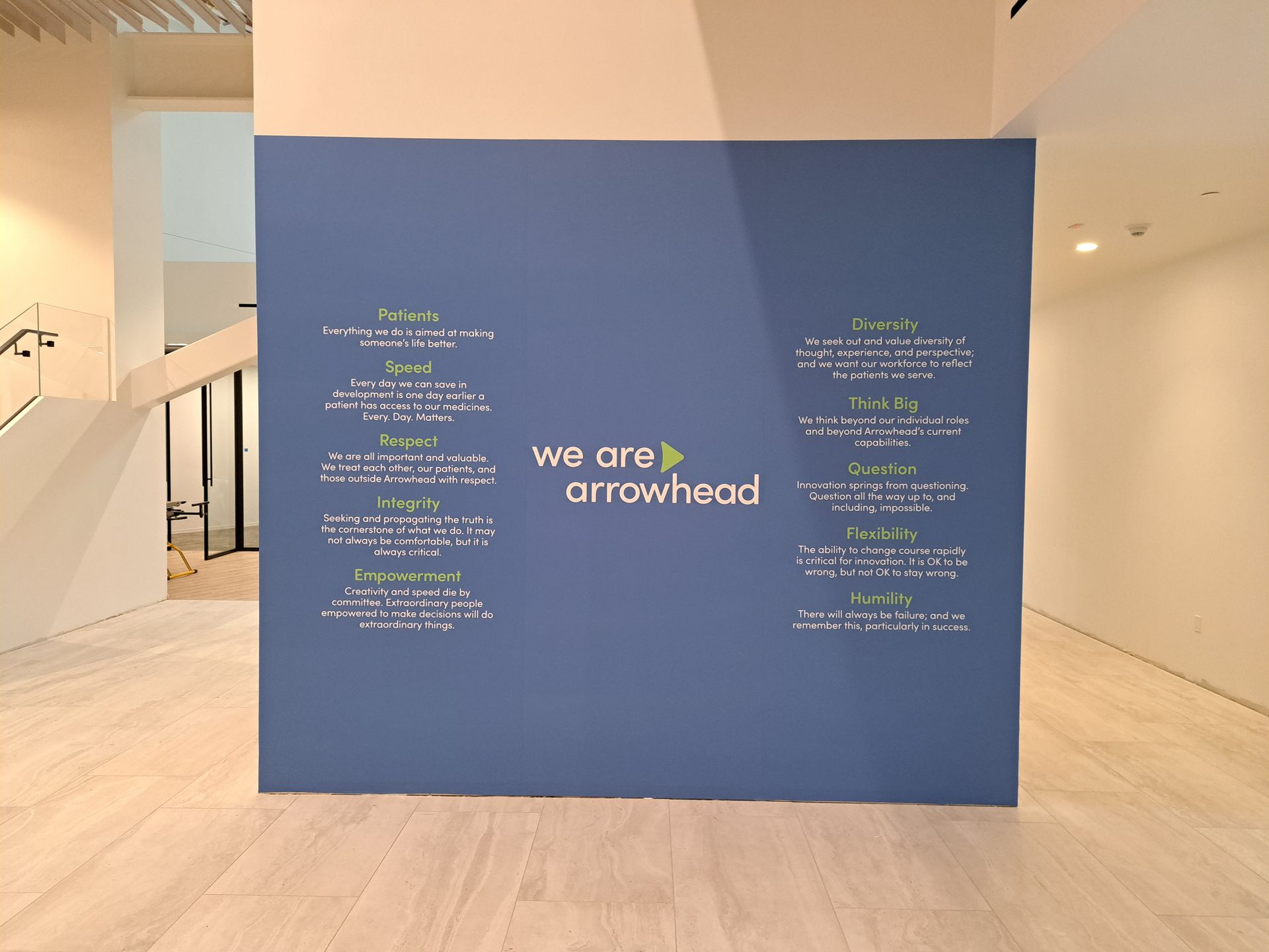 Blue wall display in a bright lobby with “we are arrowhead” and handwritten notes on both sides