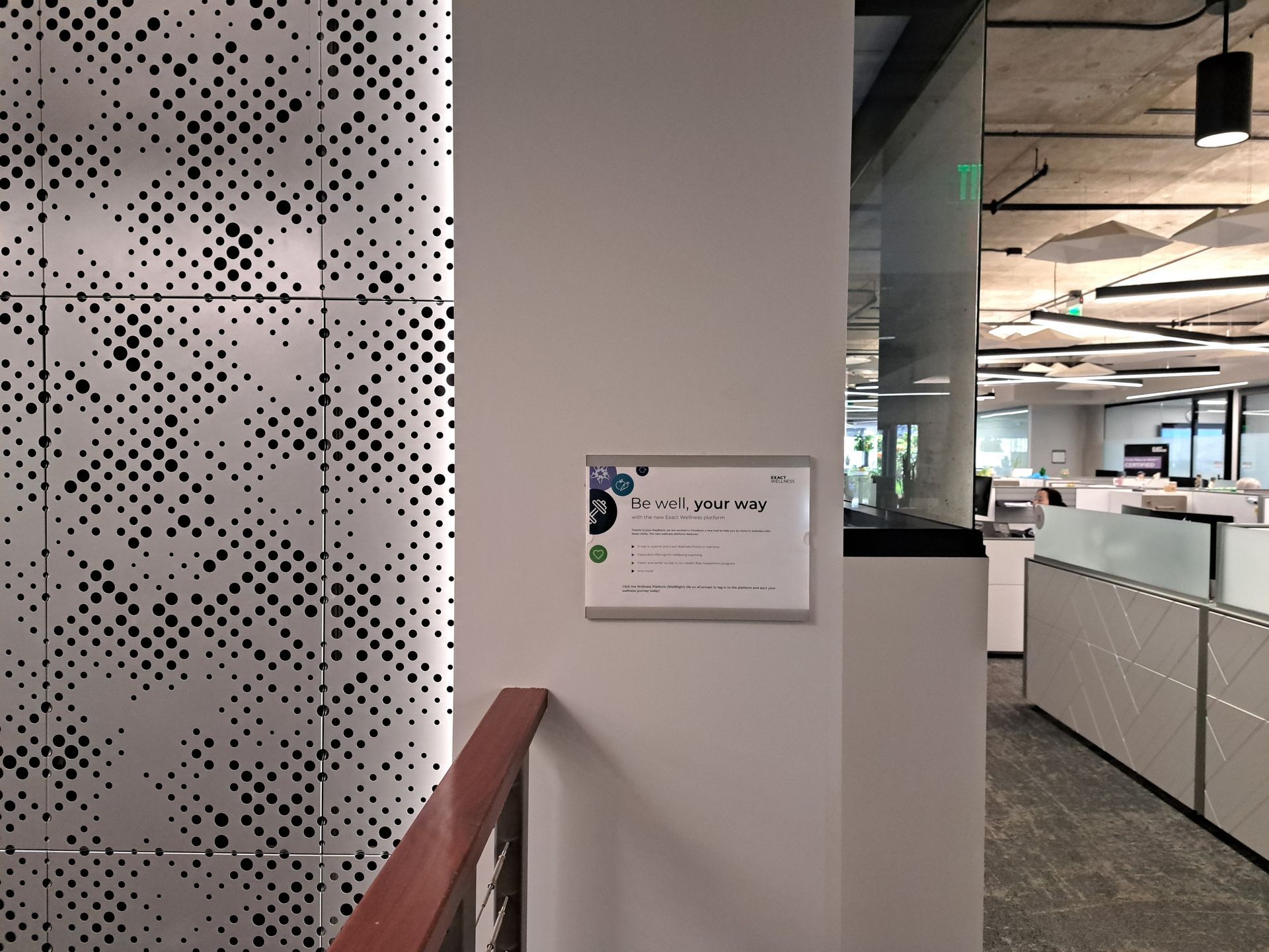 Office hallway with a wall sign beside a patterned partition and open workspace beyond.