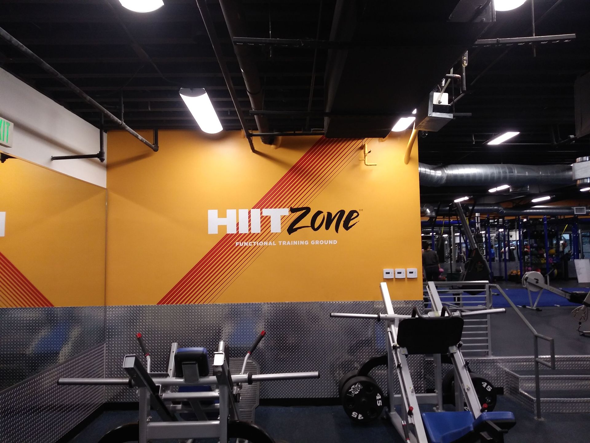 HIIT Zone gym wall with orange and black decor, workout equipment, and a person exercising on the right