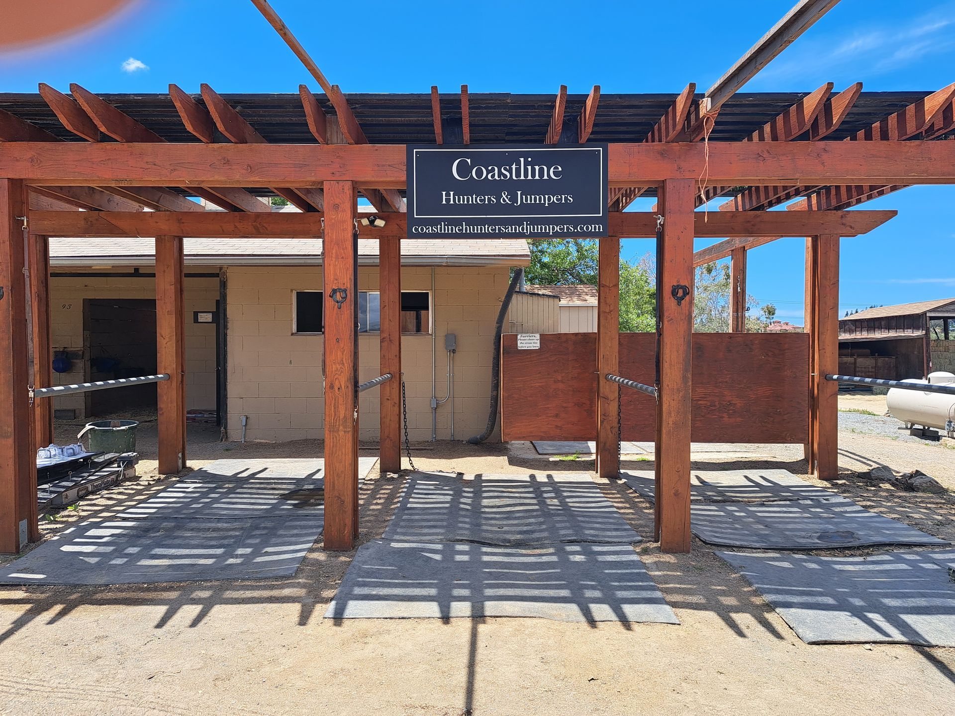 Entrance to a rustic building with a wooden pergola and sign under a clear blue sky