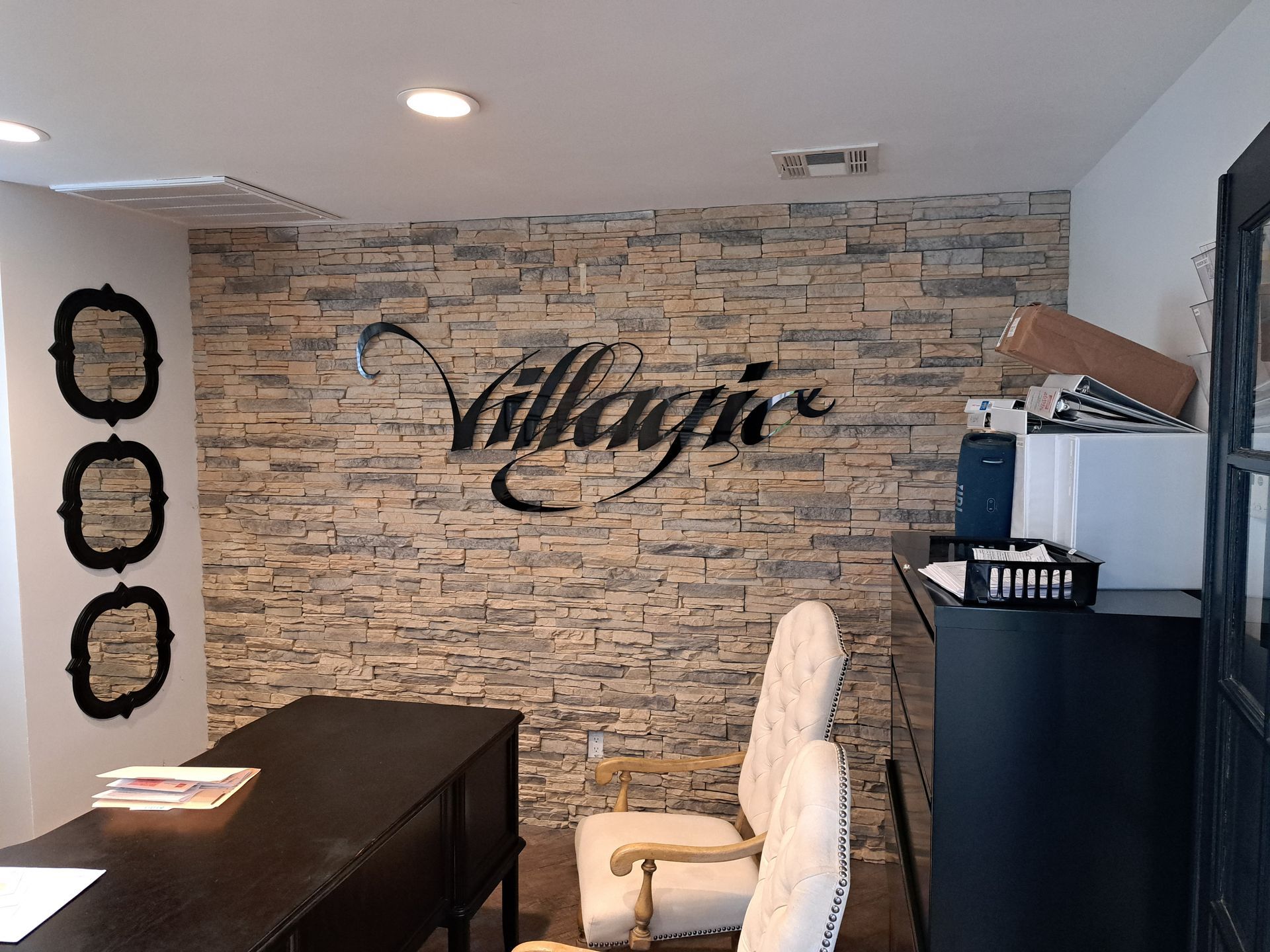 Lobby reception desk with stone accent wall, black desk, white chair, and decorative signage.