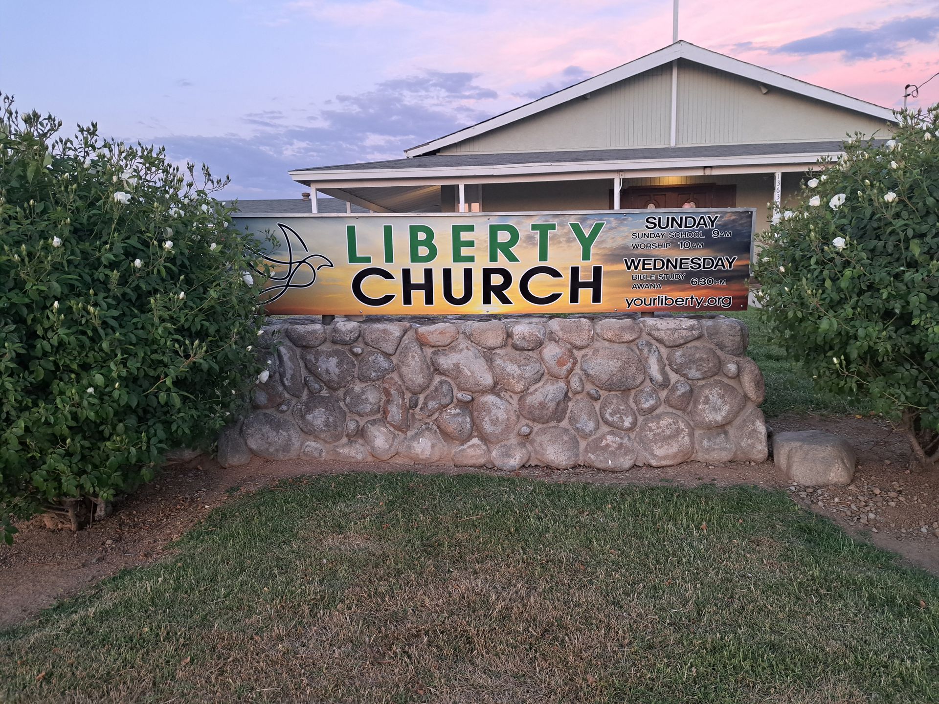 LIBERTY CHURCH sign on a stone wall in front of a building at dusk