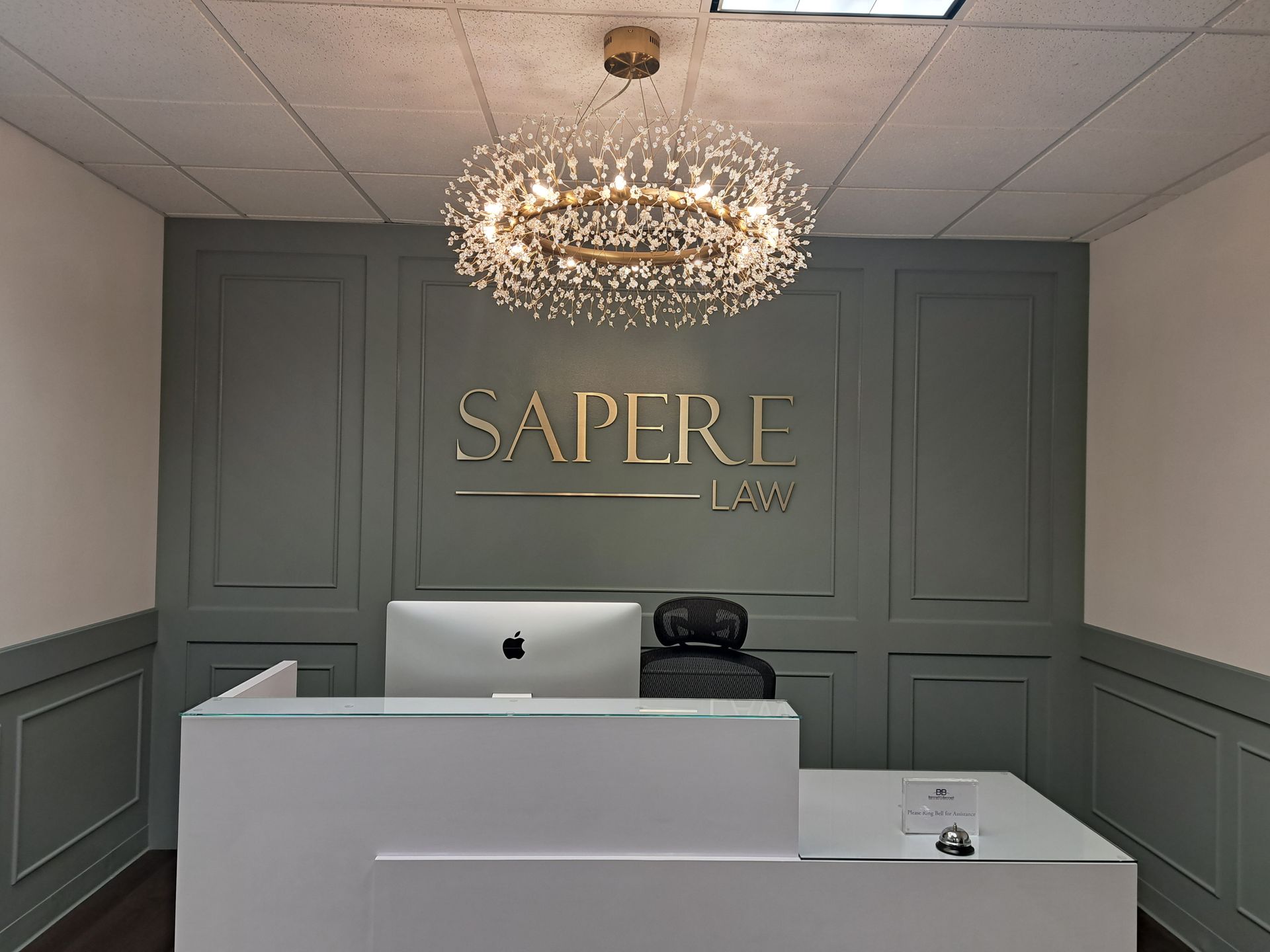 Chic reception desk with gray paneled walls, a crystal chandelier, and a gold “SAPRE” sign