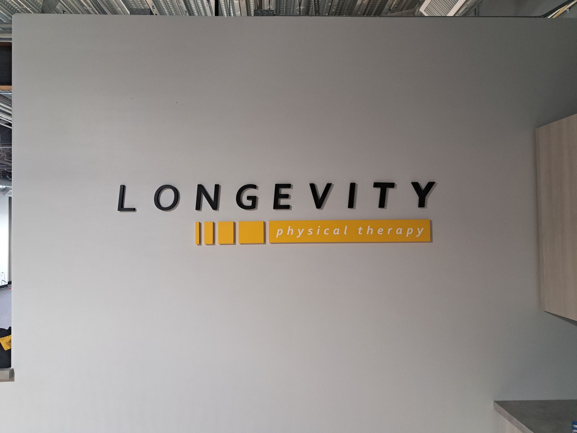 Wall sign reading “LONGEVITY” with a gold “advanced therapy” logo on a gray wall