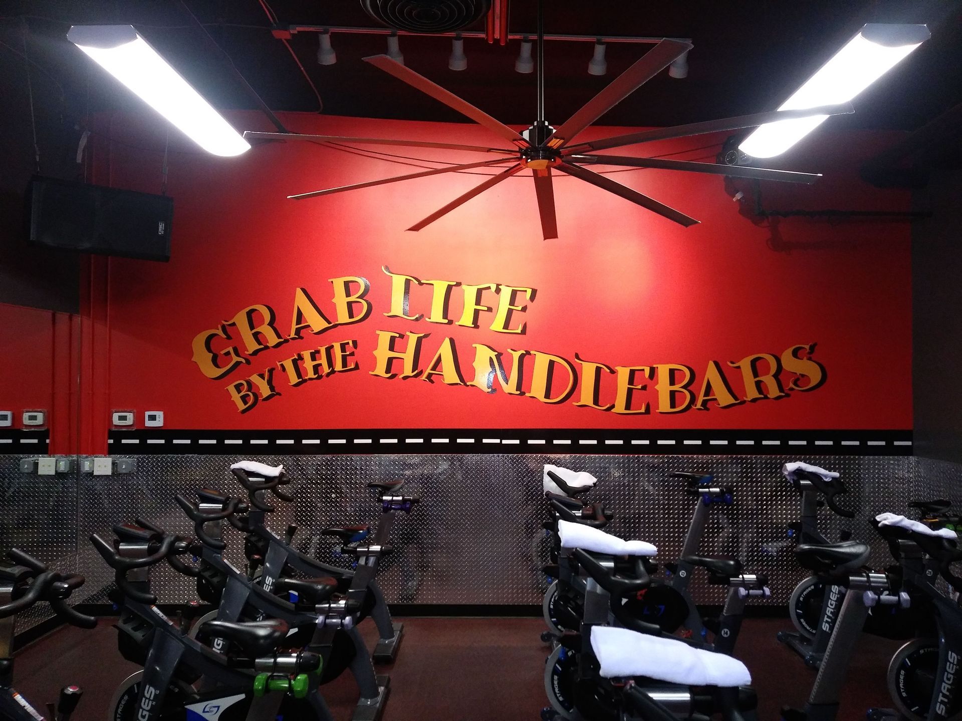 Indoor cycling studio with red walls and slogan “GRAB LIFE BY THE HANDLEBARS” above rows of bikes.