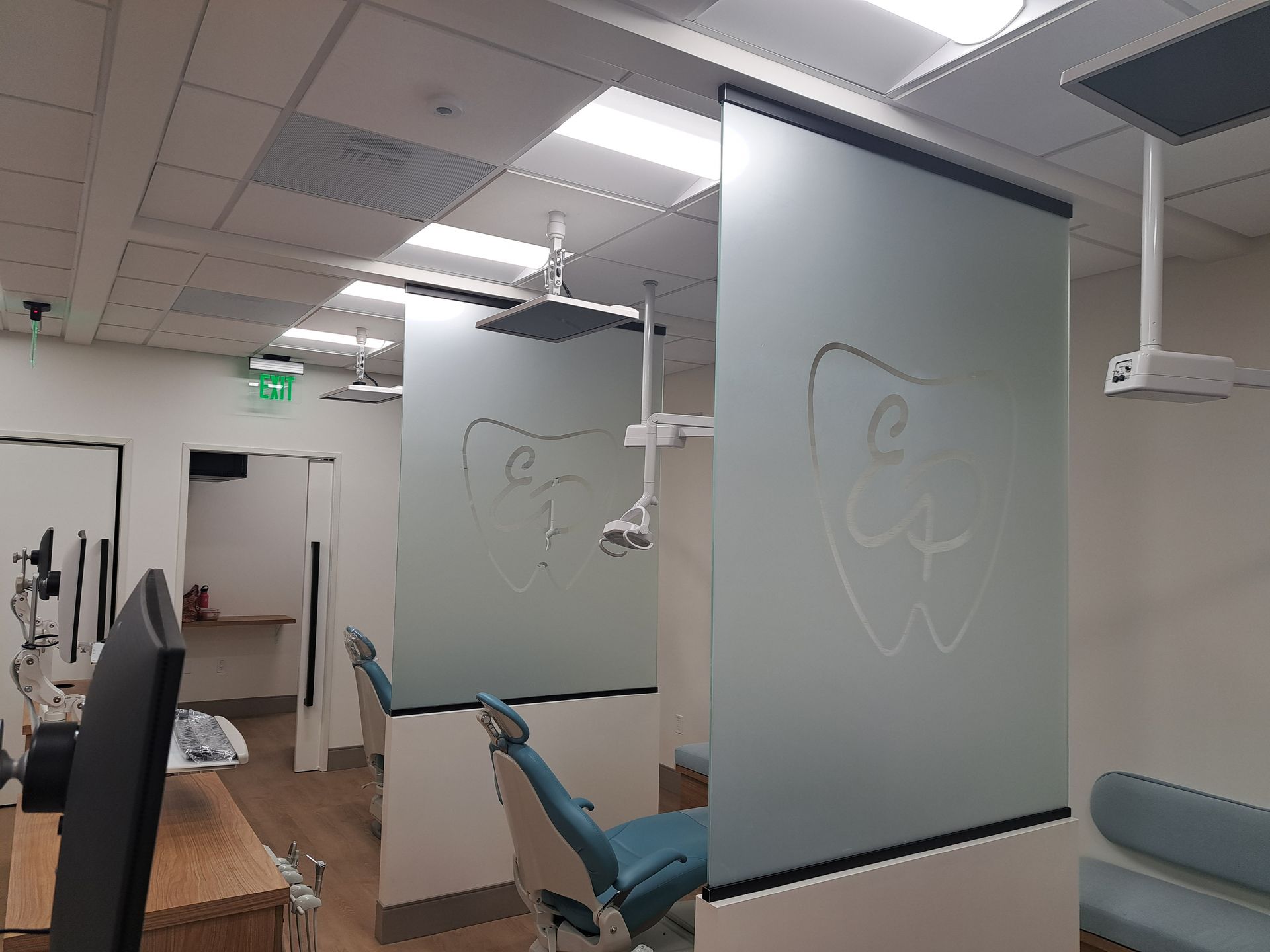 Dental clinic with frosted glass partitions, exam chairs, and ceiling-mounted dental lights.