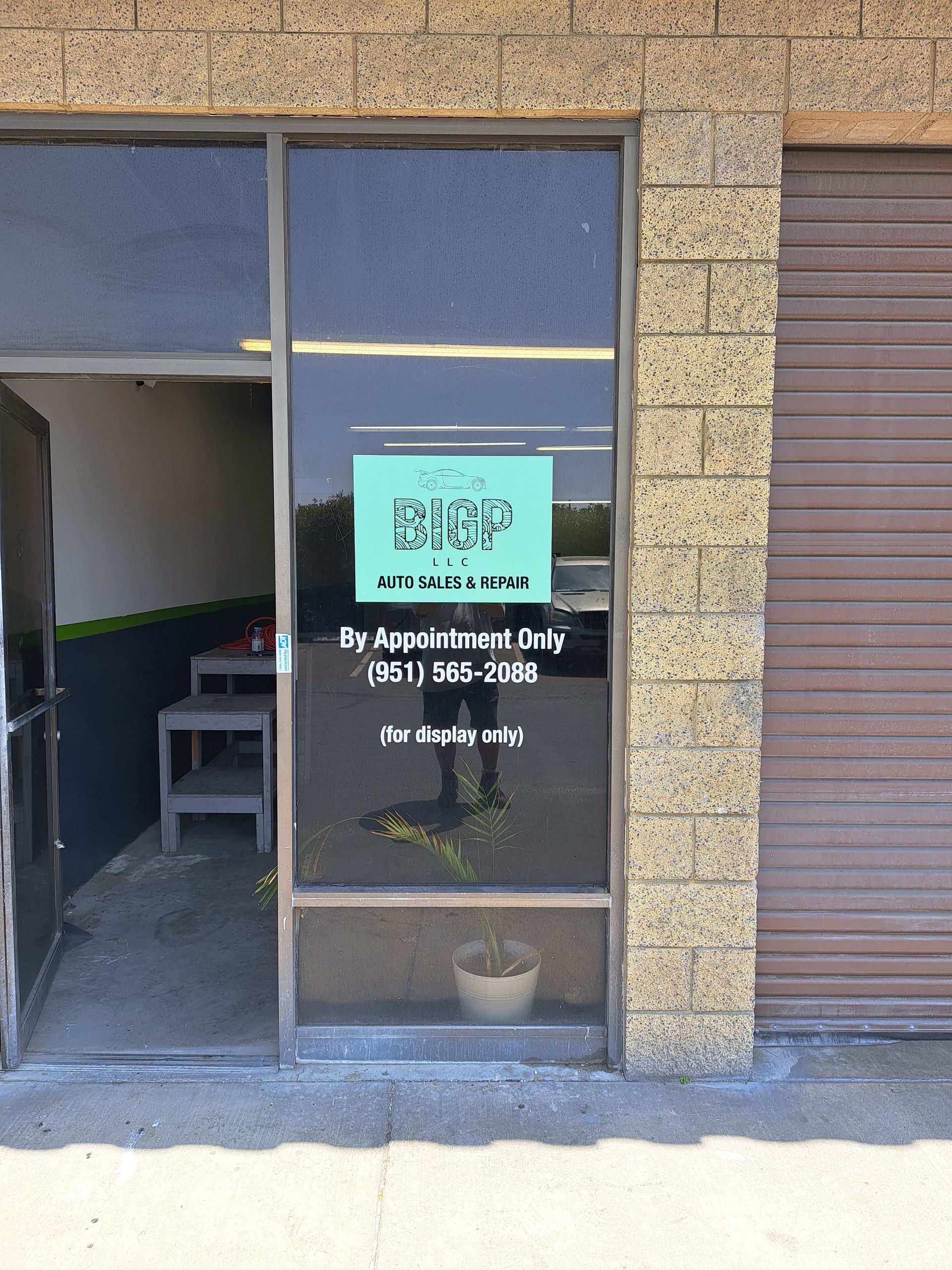Storefront with open door, glass sign, and roll-up shutter on a brick building.