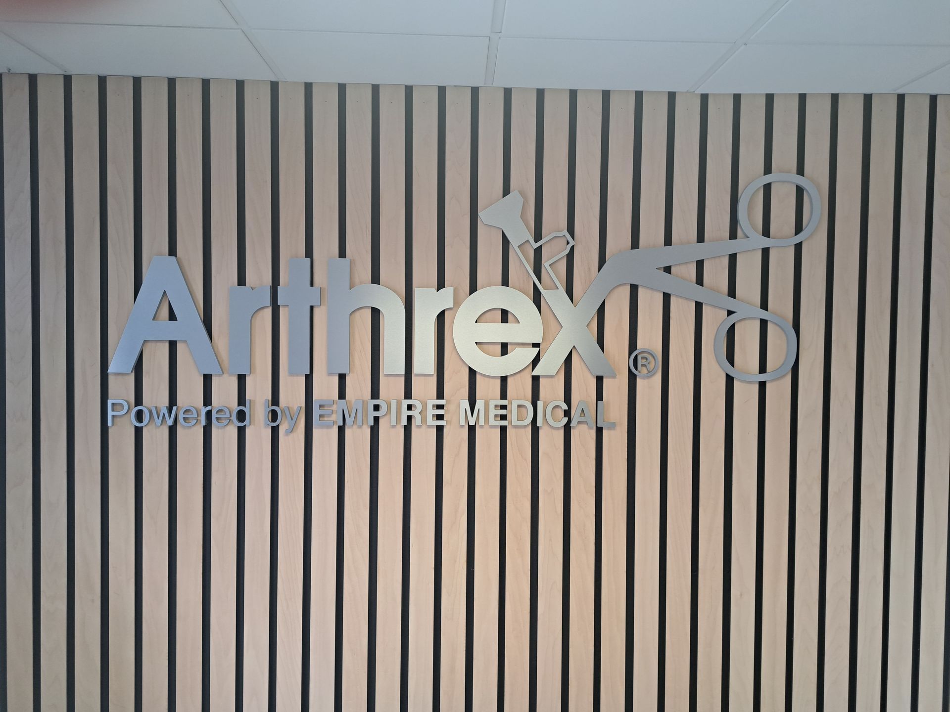Arthrex logo on a vertical wooden slat wall with the tagline “Powered by Procedure.”
