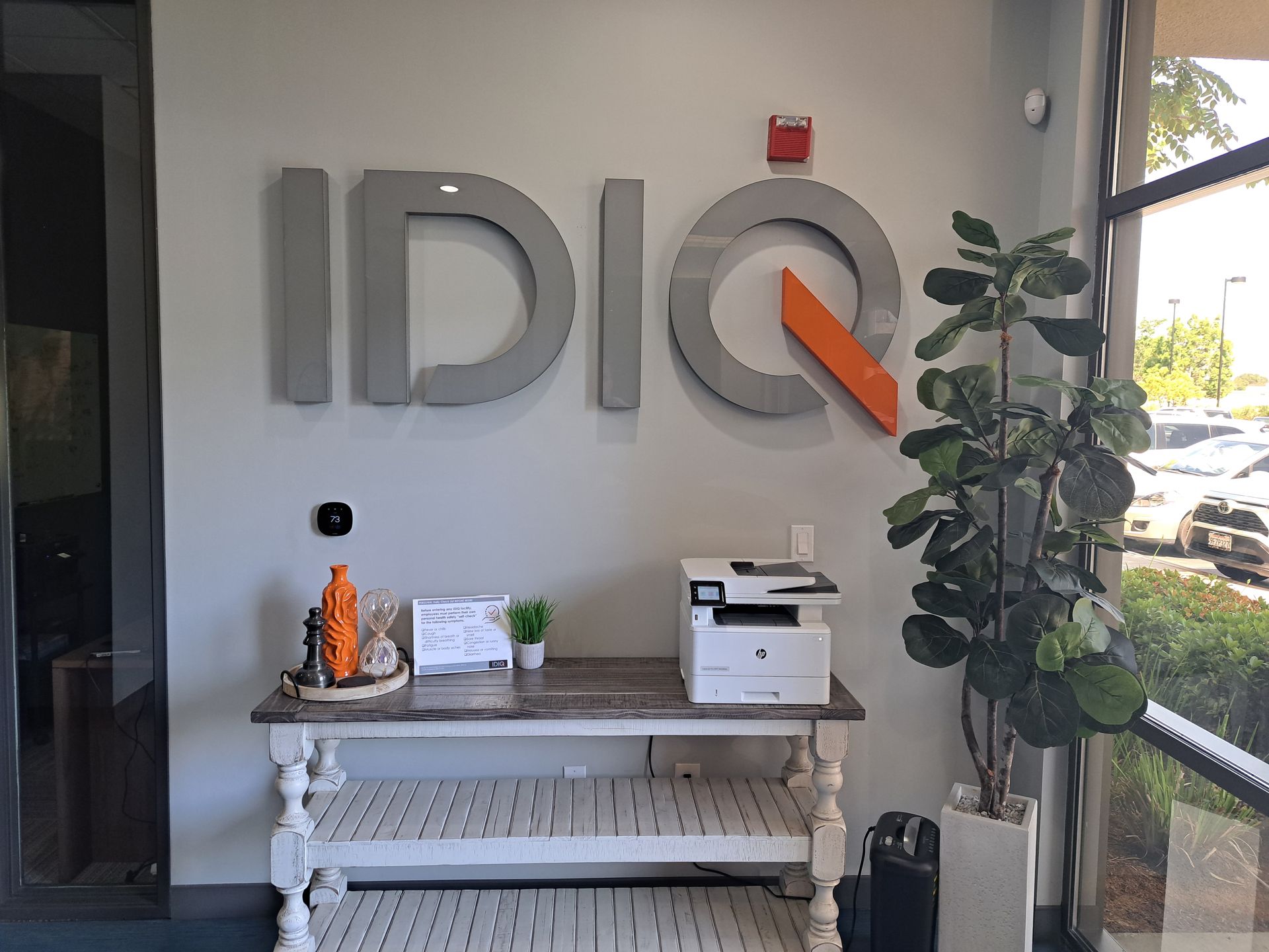 IDIQ office lobby with large wall logo, console table, plant, and printer by a glass door