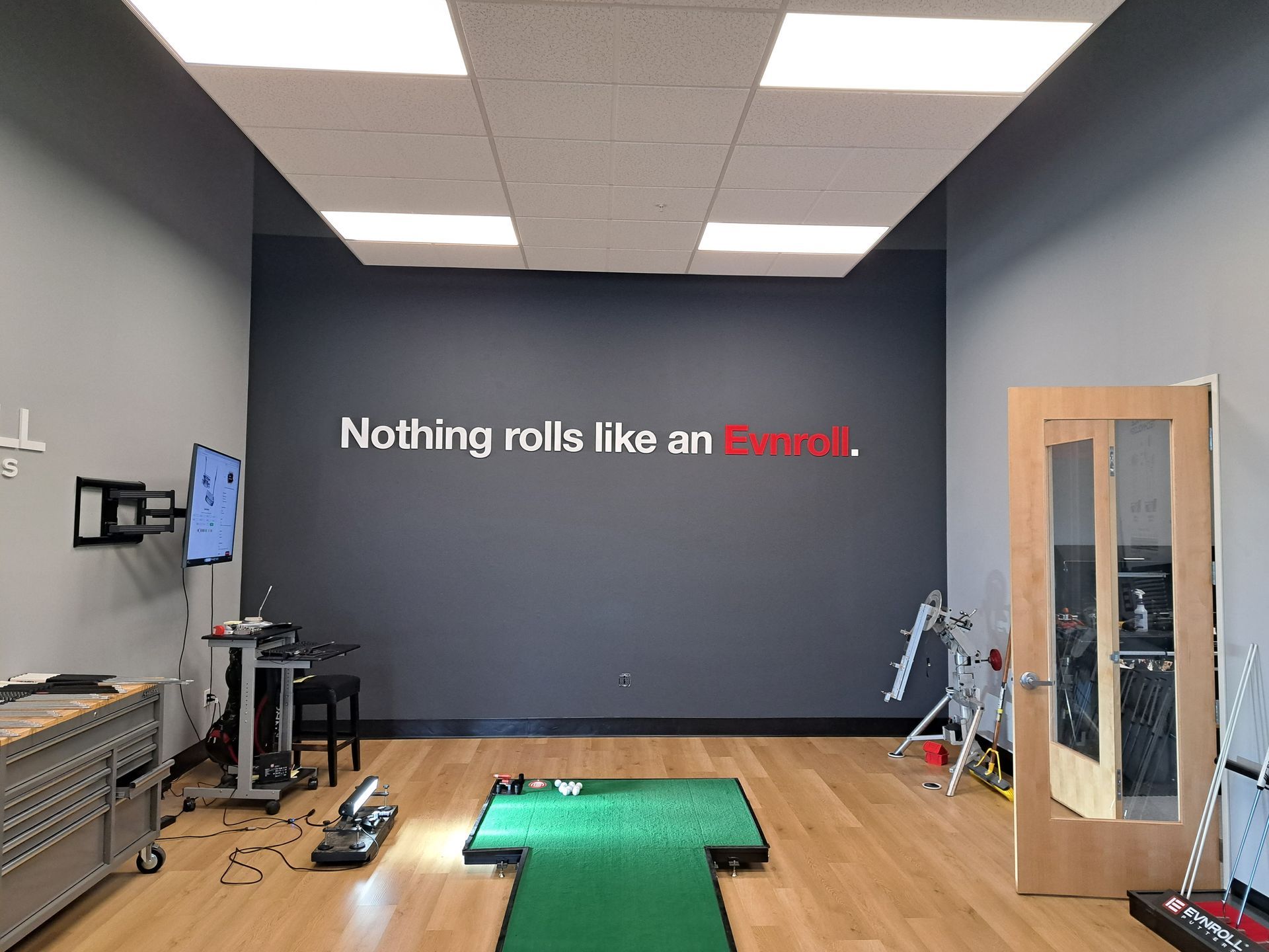 Indoor training room with a treadmill on green turf and a wall sign reading “Nothing rolls like an Envroll.”