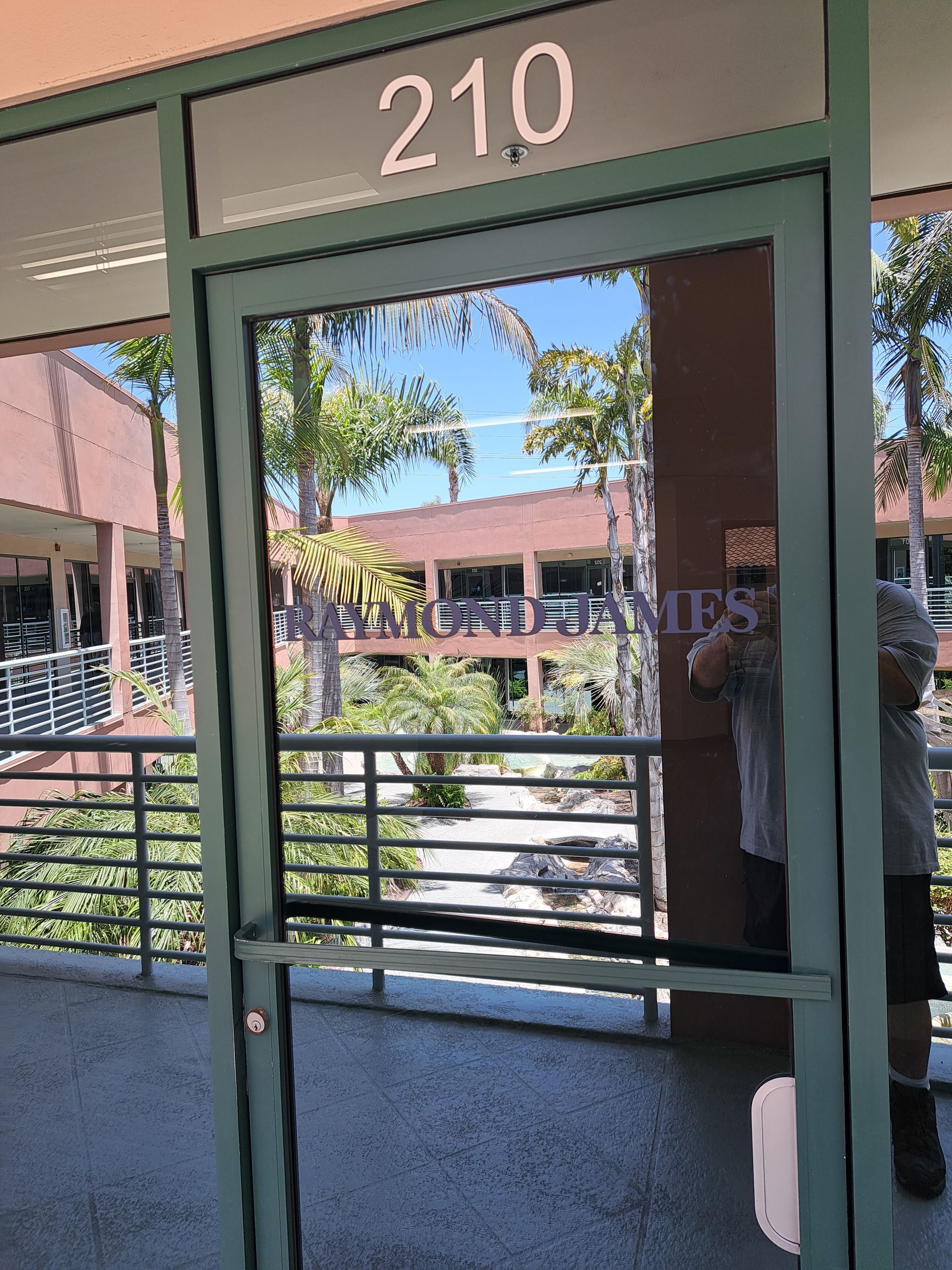 Glass door marked “210” with a view into a courtyard and building beyond.