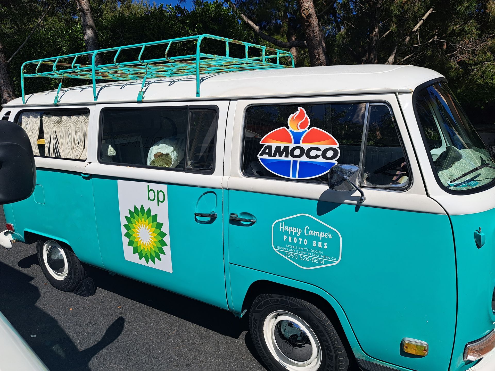 Turquoise-and-white vintage van with roof rack and AMOCO sign parked on a street.