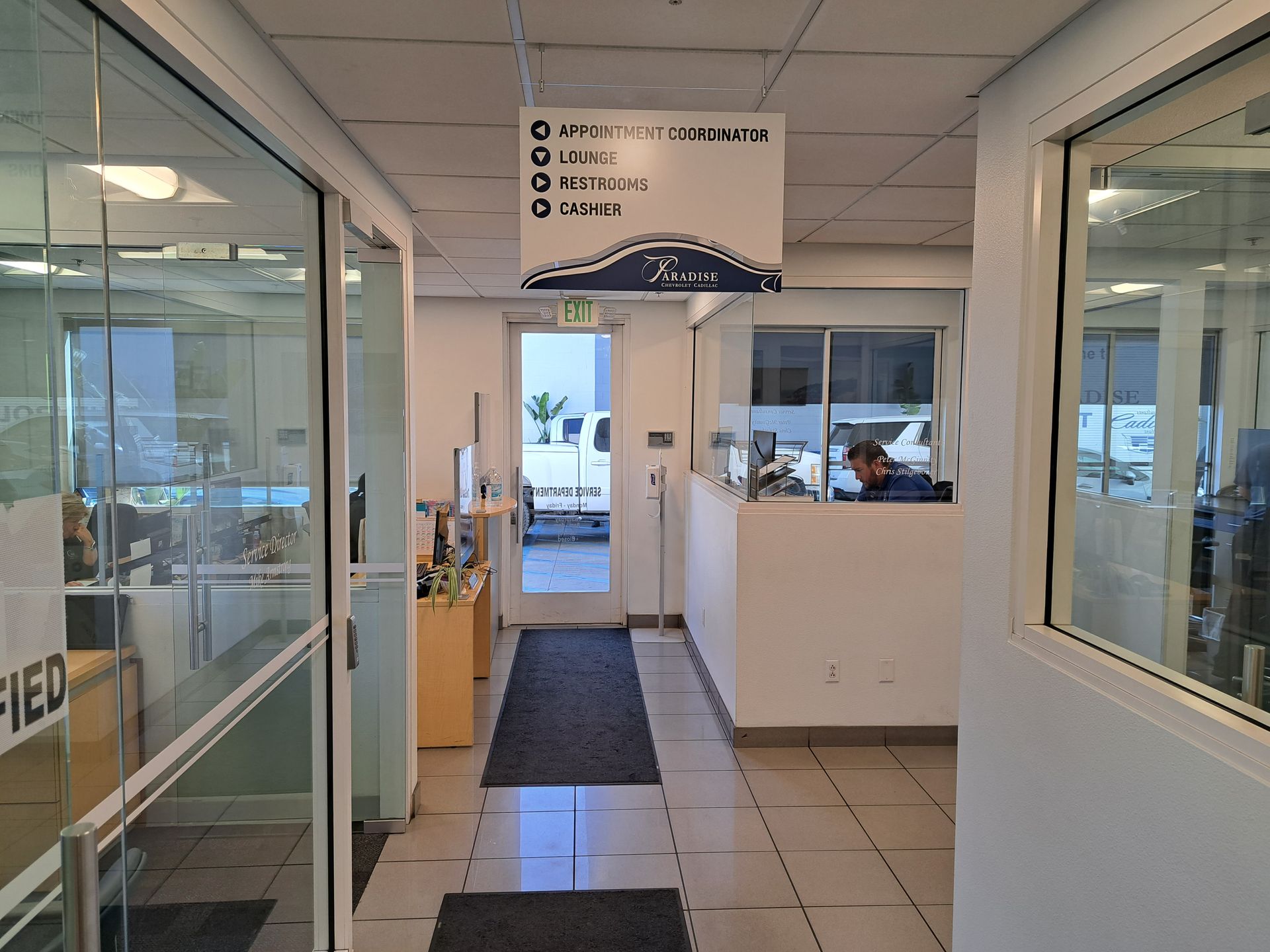 Bright office hallway with glass windows and doors, tiled floor, and a sign overhead.