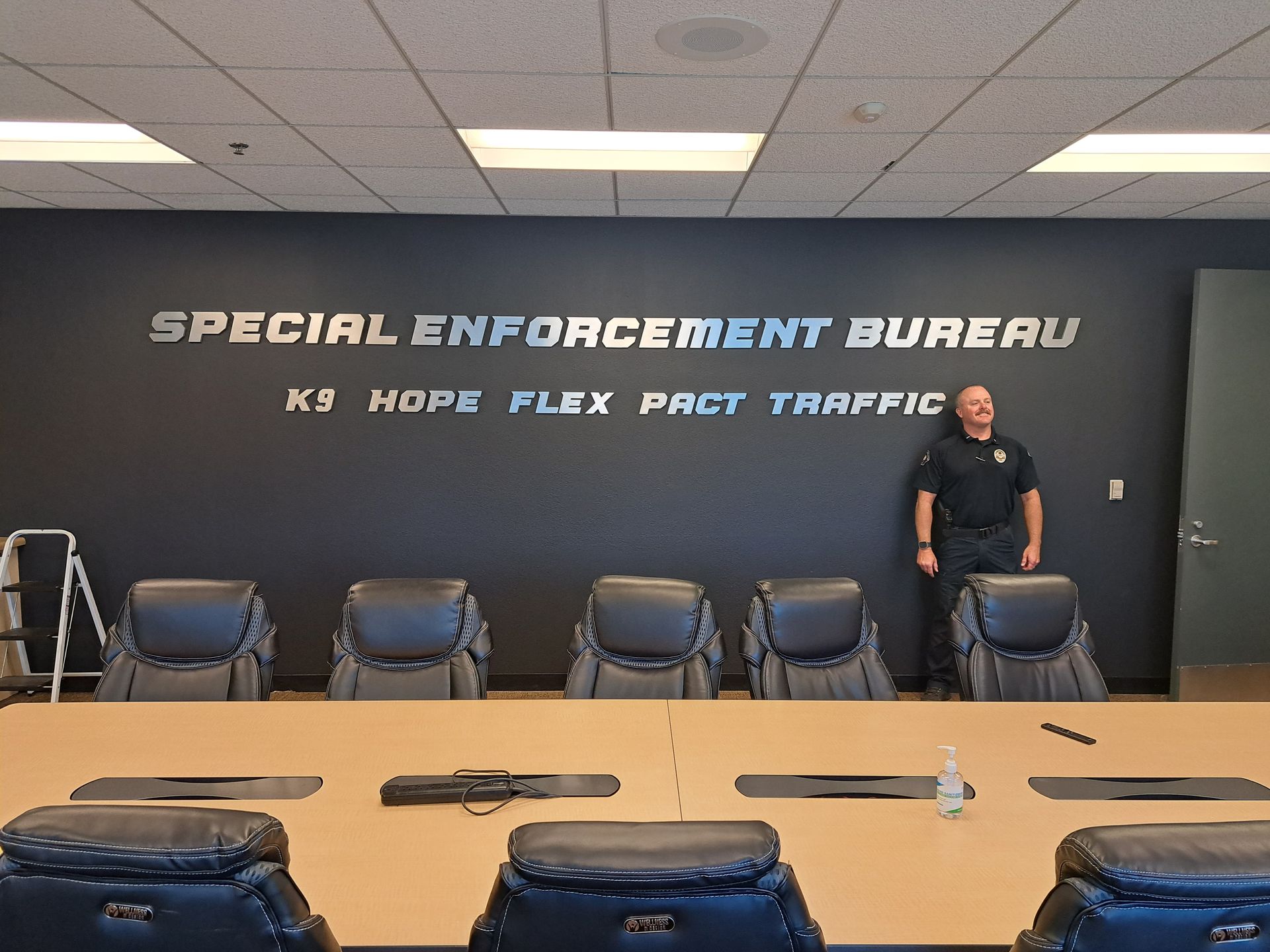 Special Enforcement Bureau wall behind table and chairs, with a person standing at the right side of the room