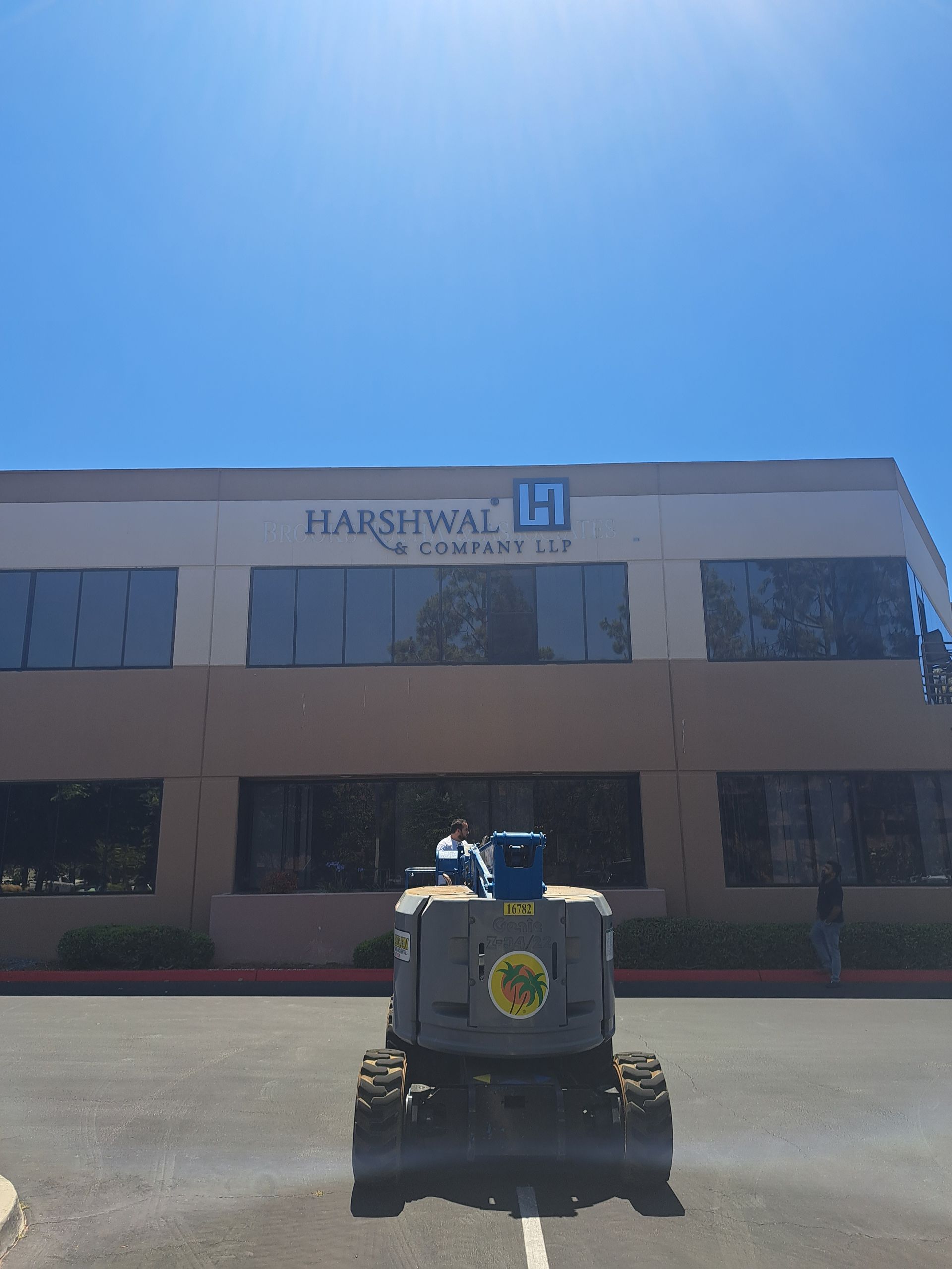Small utility vehicle parked outside a Harshwa building under a bright blue sky.