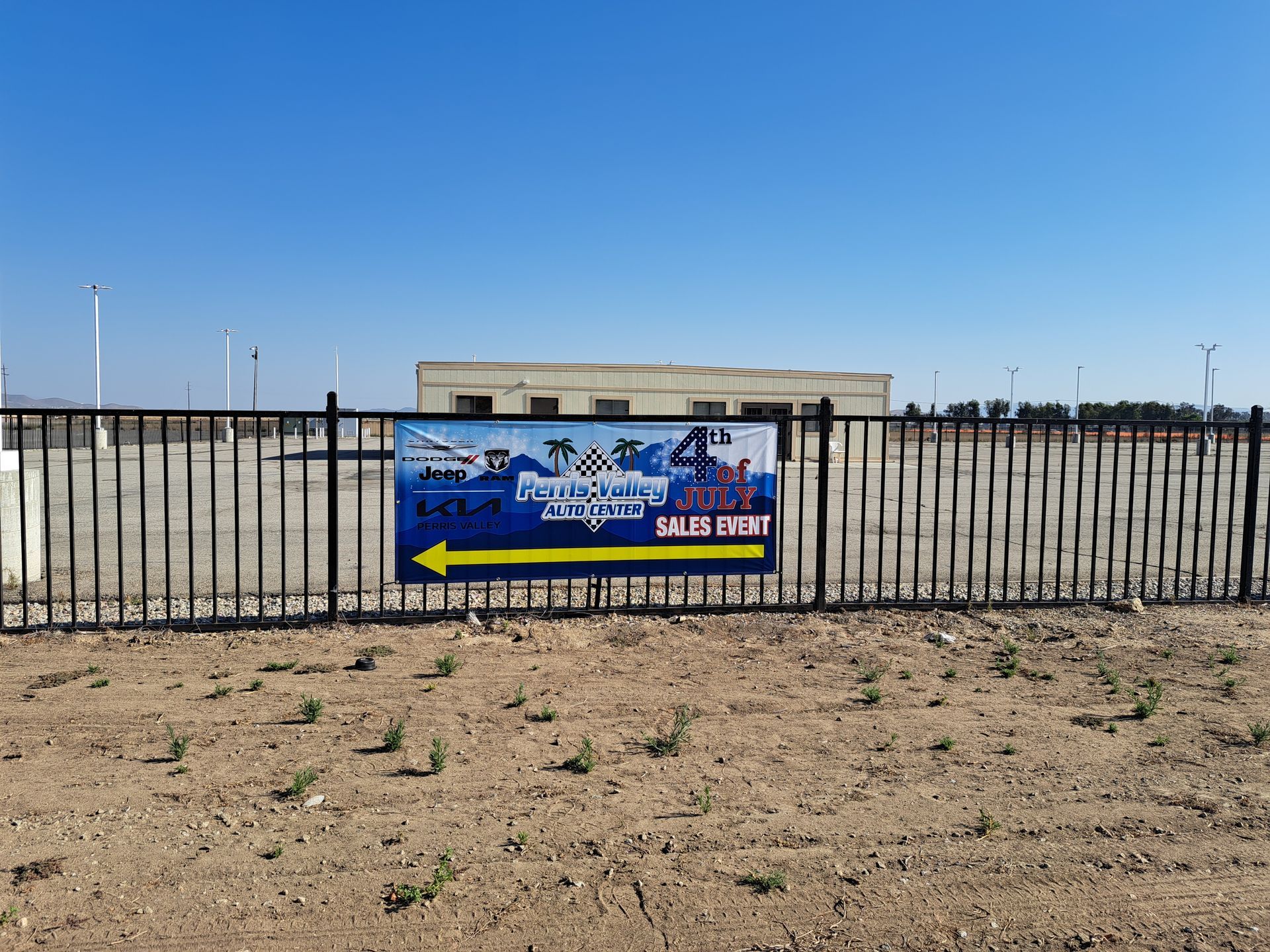 Blue sign on a black fence in a barren field, with yellow arrows pointing left and right.