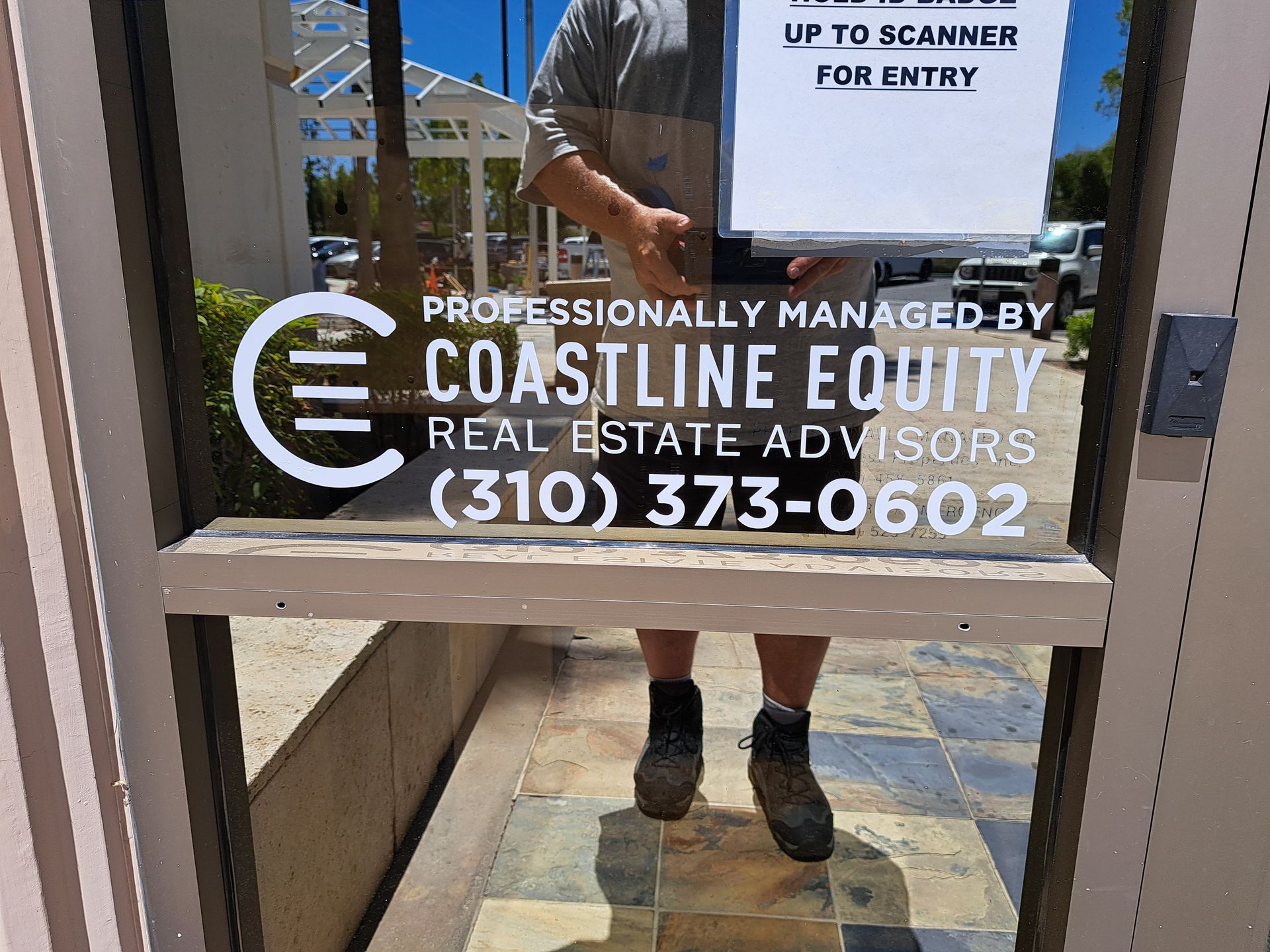 Glass door sign for Coastline Equity real estate advisors with phone number and scanner notice