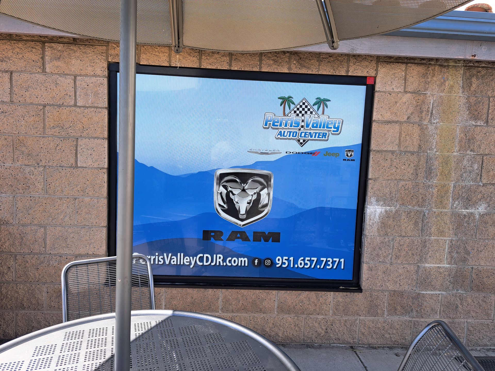Blue promotional banner on a brick wall with a Ram logo and dealer contact info under an awning