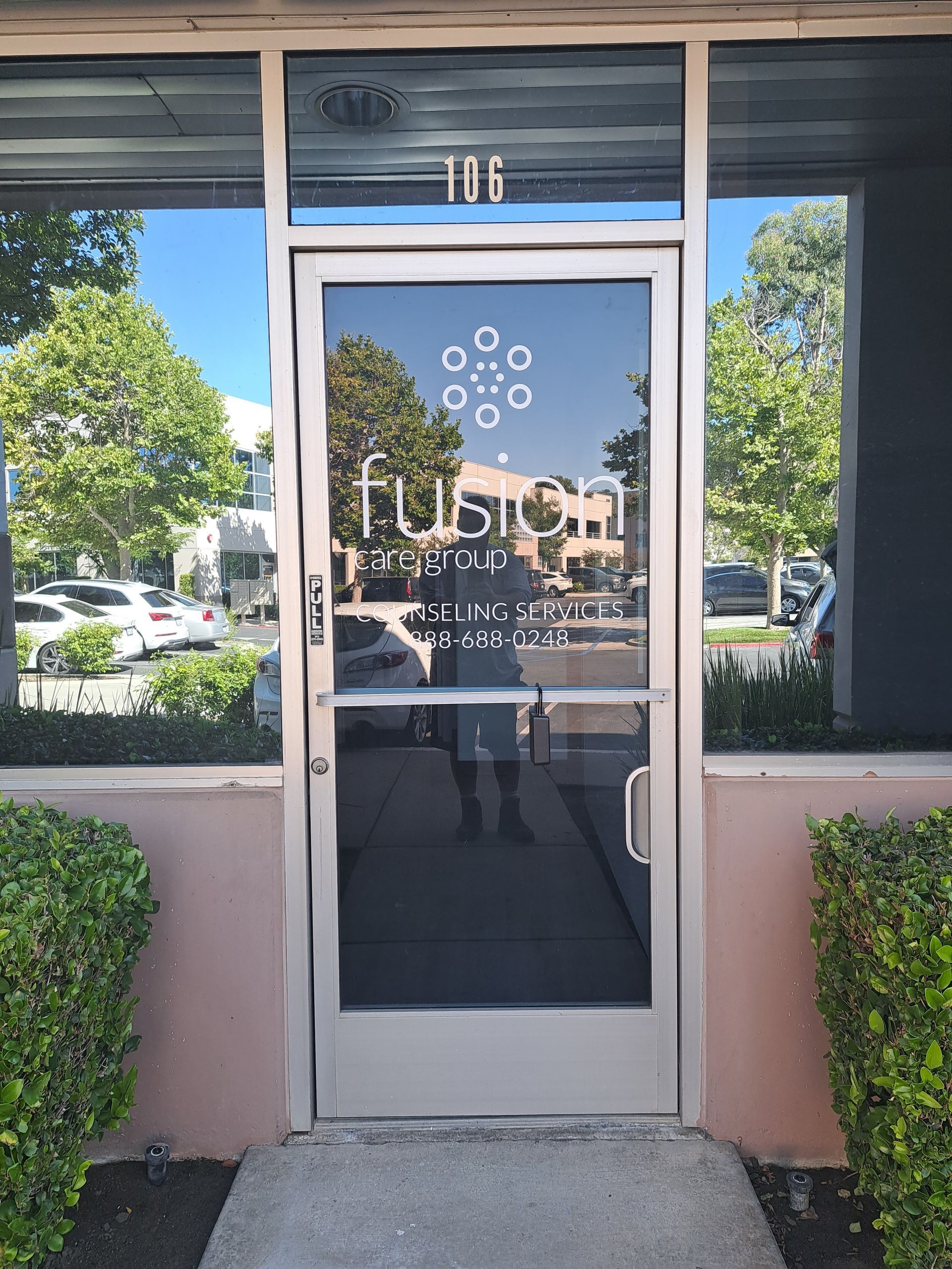 Glass storefront entrance with “Fusion” signage, framed by pink walls and greenery on either side