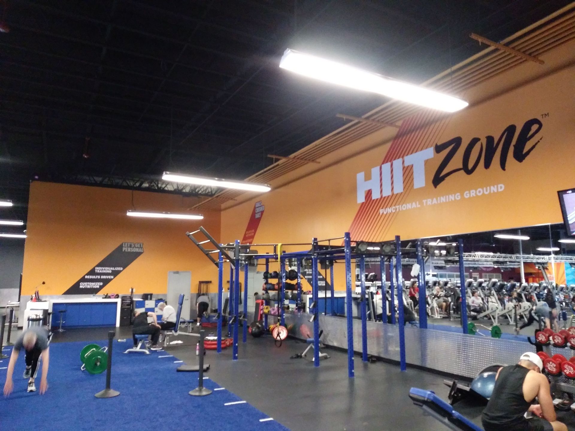 HIIT Zone gym interior with blue turf, exercise equipment, and people training under bright lights
