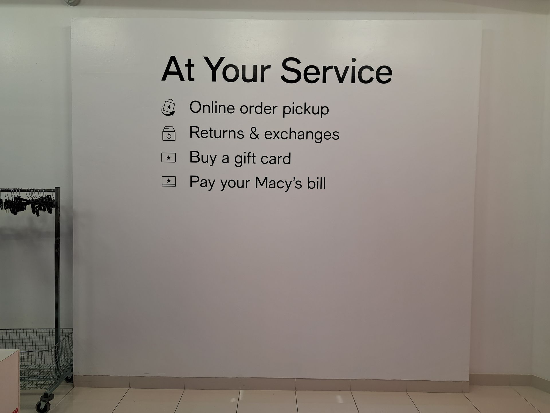 Macy’s service desk sign listing online order pickup, returns and exchanges, gift cards, and bill payment