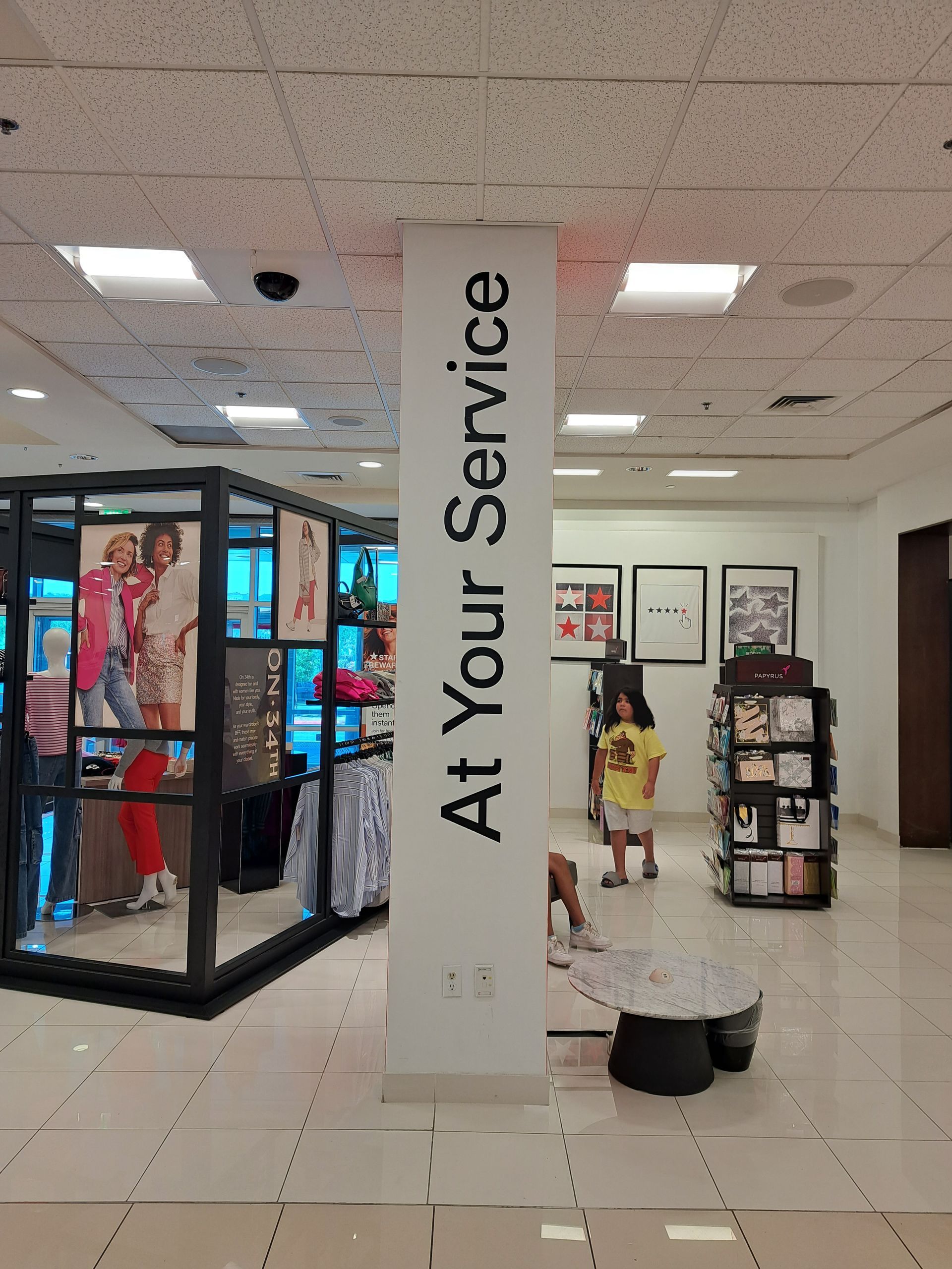 Store interior with “At Your Service” pillar sign and clothing displays in the background
