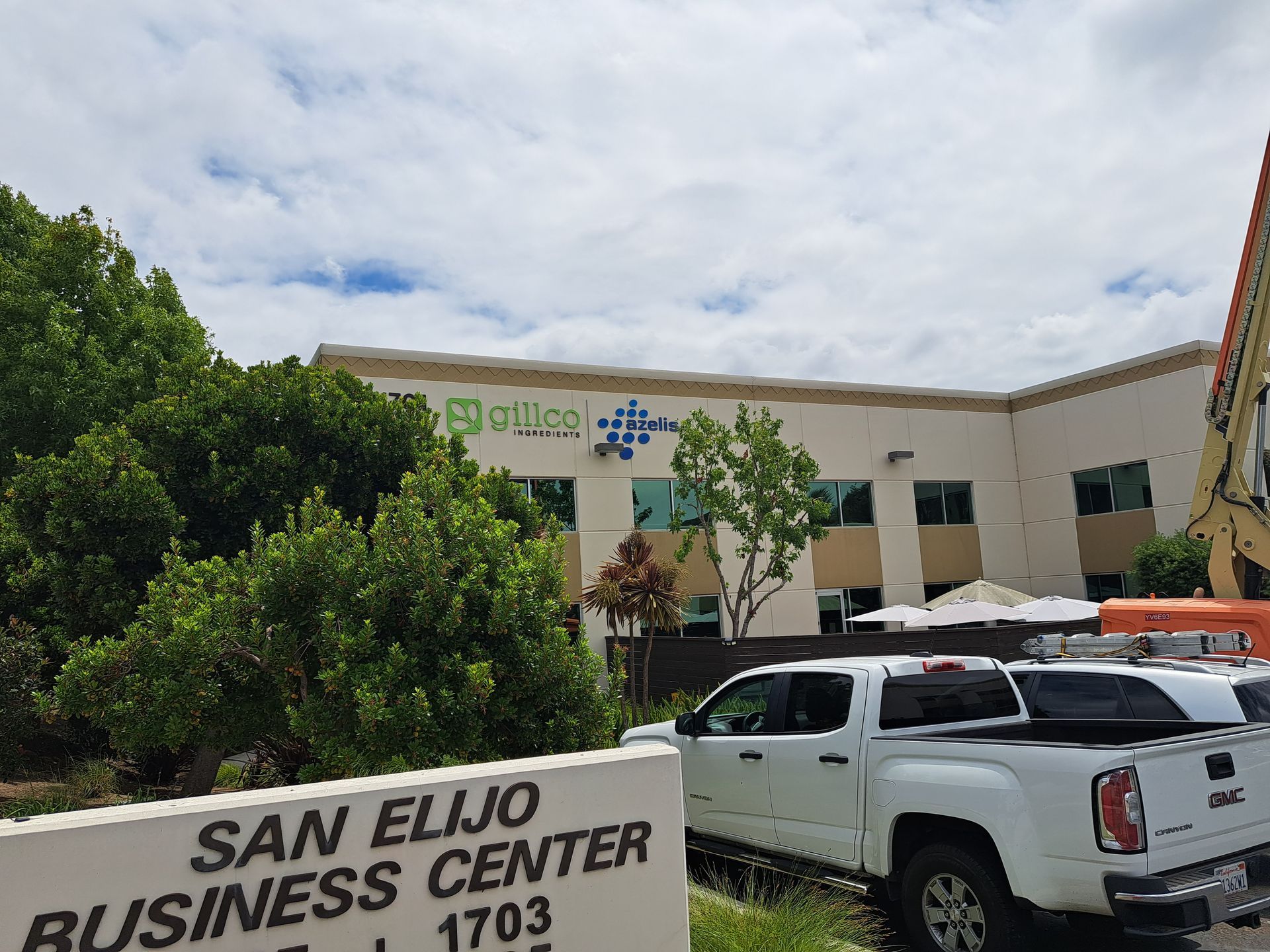 San Elijo Business Center building with parked white trucks, trees, and cloudy sky