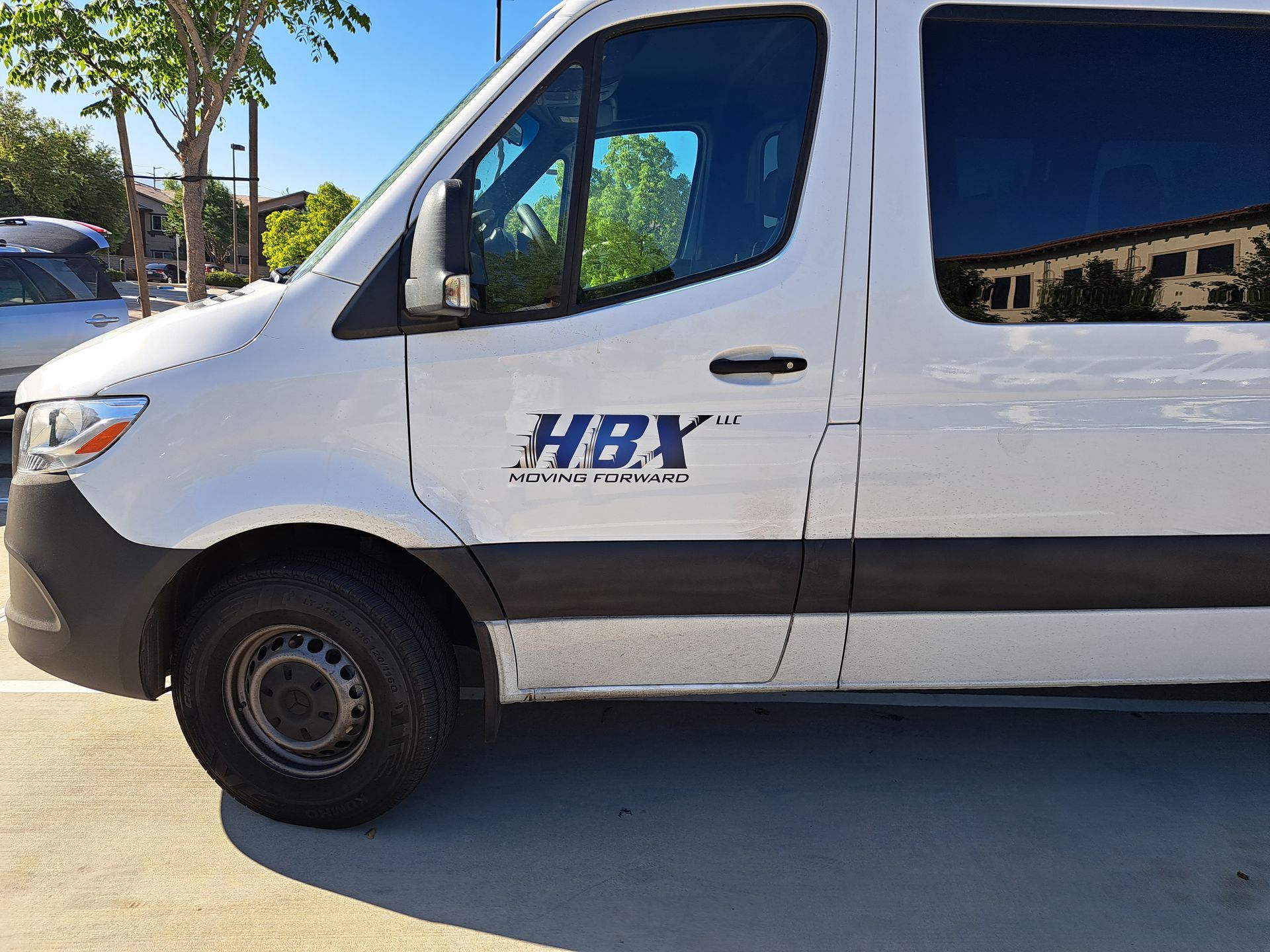 White HBI delivery van parked on a sunny street, side view with trees and buildings in the background