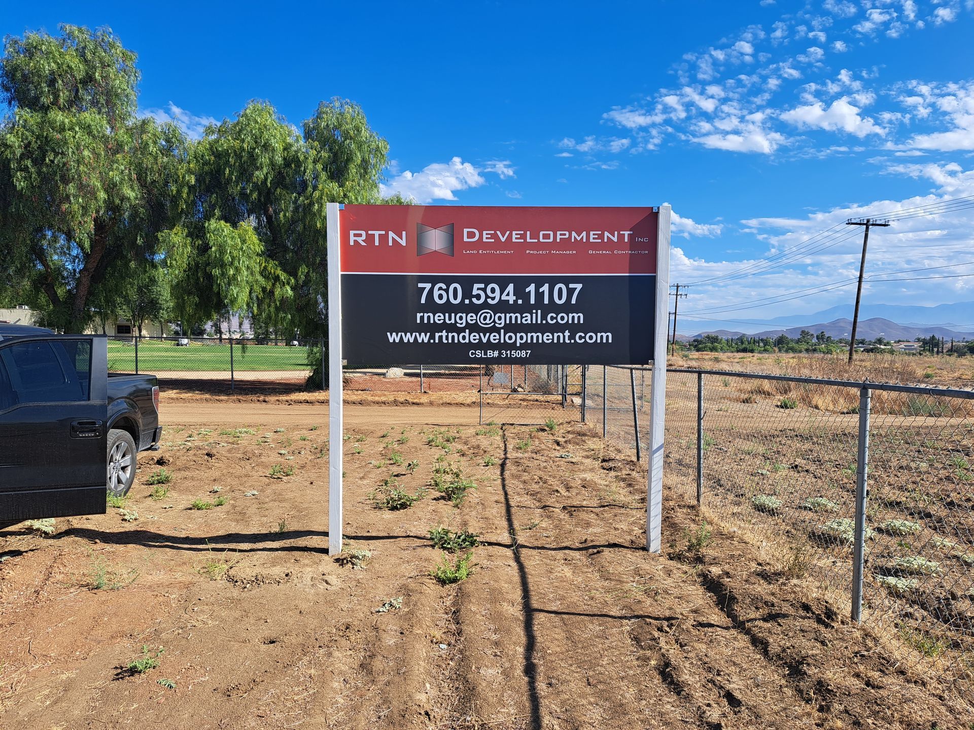 Real estate sign by a dirt road in a rural area with trees and blue sky