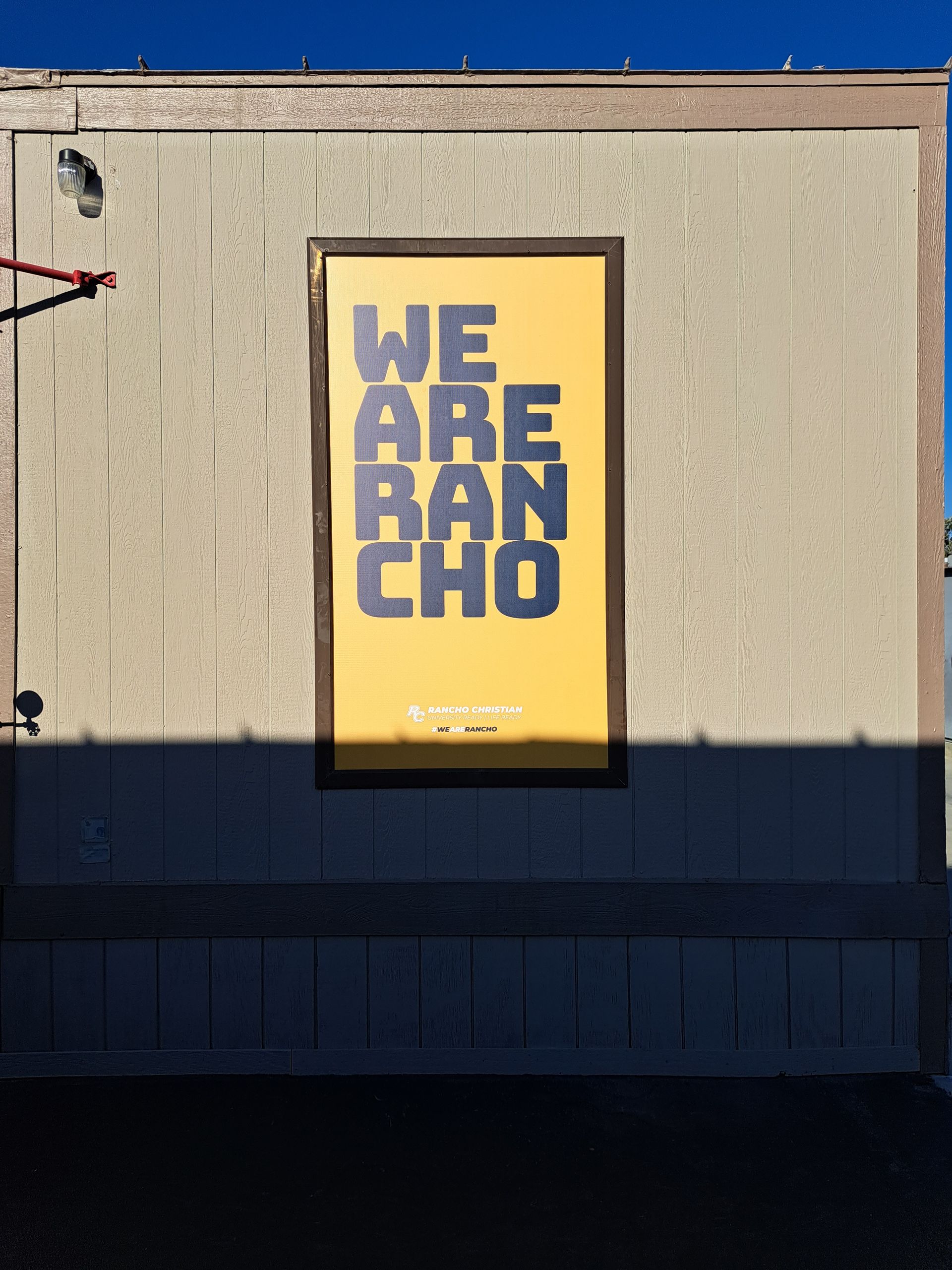 Poster on a beige wall with bold purple text reading “WE ARE RANCHO” on a yellow background.