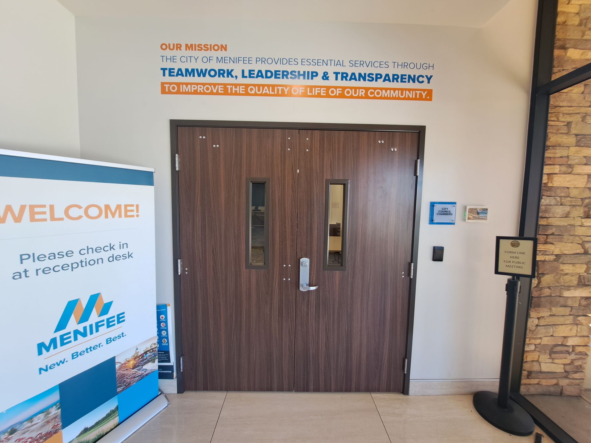Lobby entrance with wooden double doors, welcome sign, and accessibility plaque on the wall