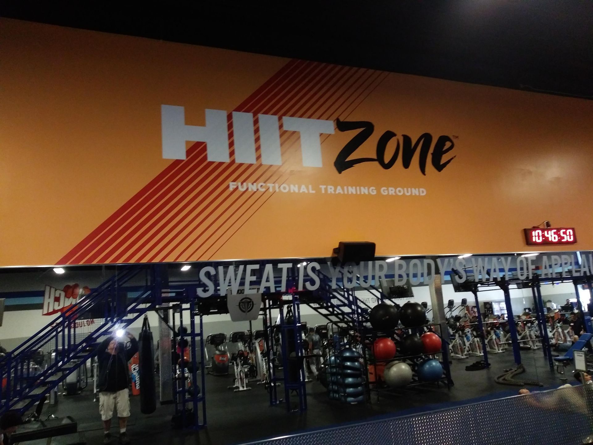 HIIT Zone gym interior with orange wall, red accents, and exercise equipment under a motivational sign