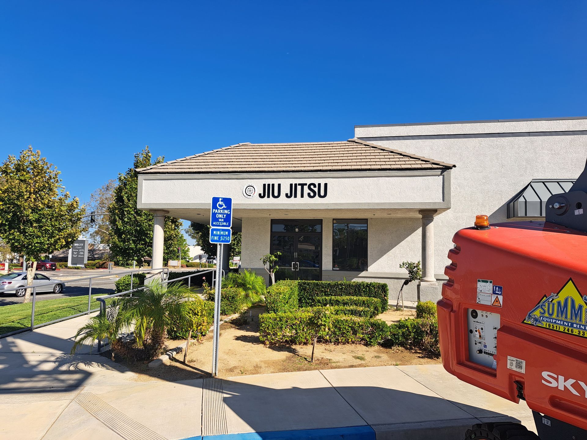 Jiu Jitsu storefront with blue handicap sign, palm shrubs, and a red vehicle in front