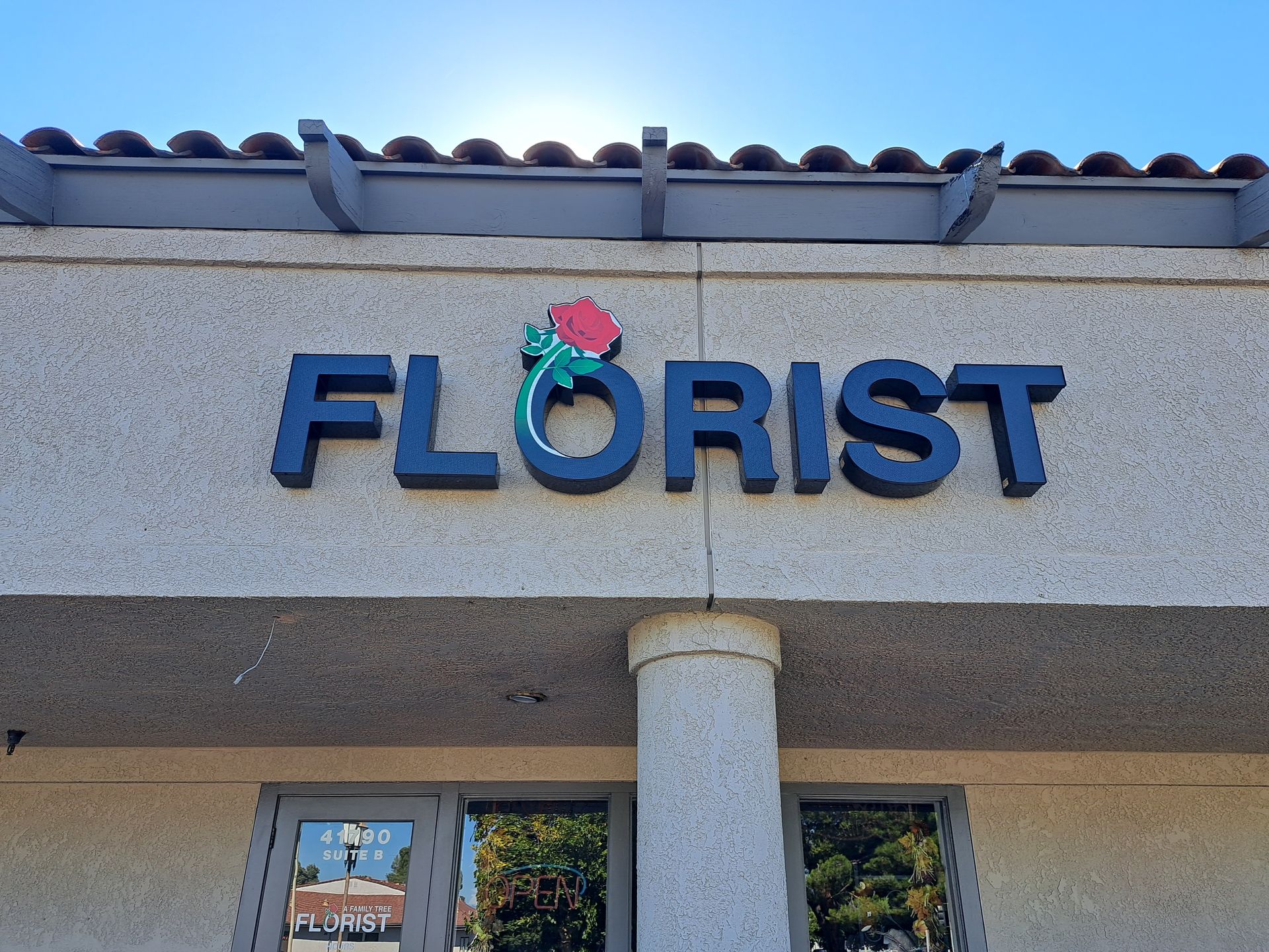 Blue “FLORIST” sign on a building facade above windows and a column